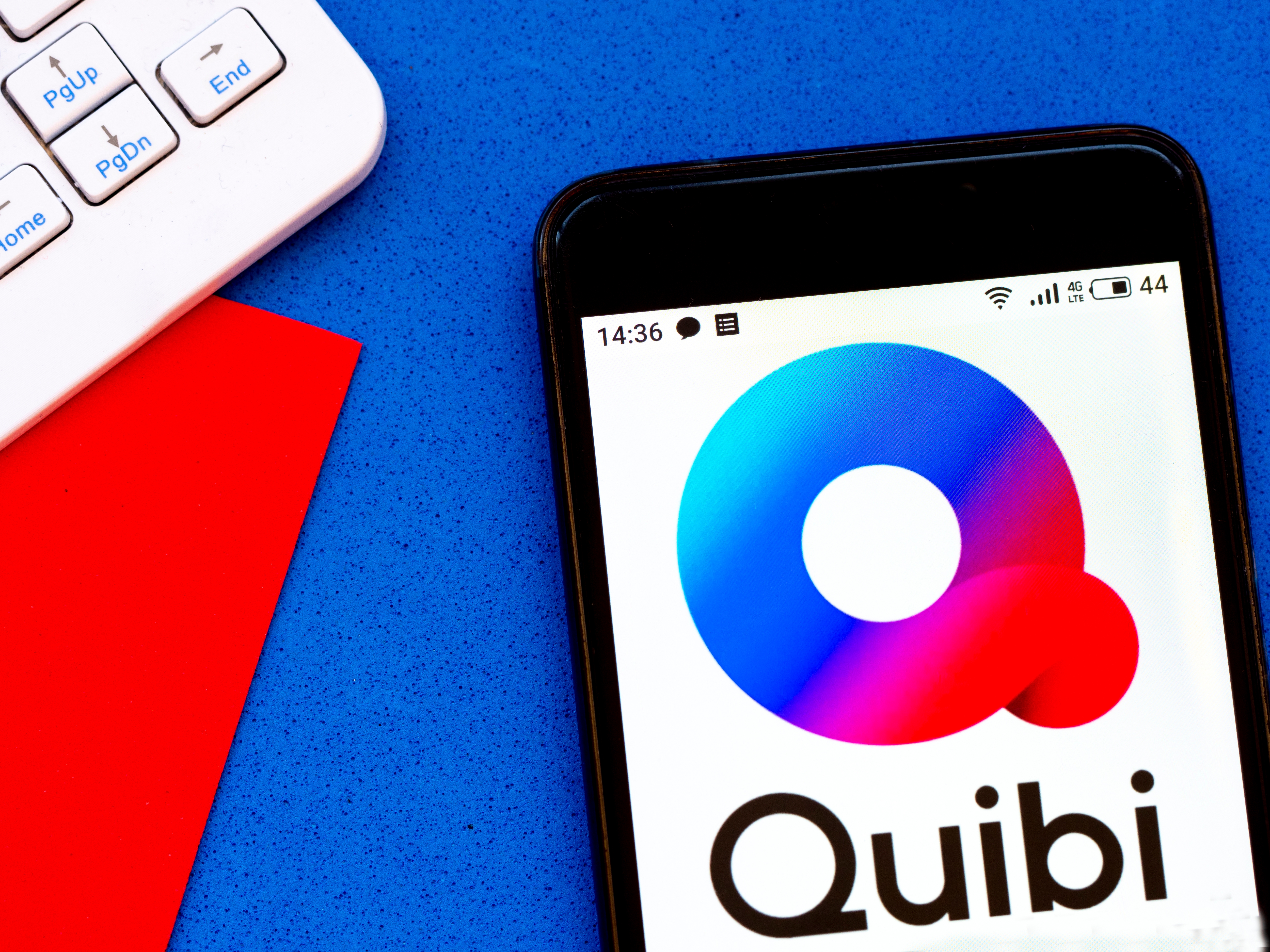 Smartphone displaying Quibi logo next to a keyboard and red paper, suggesting a tech or media context
