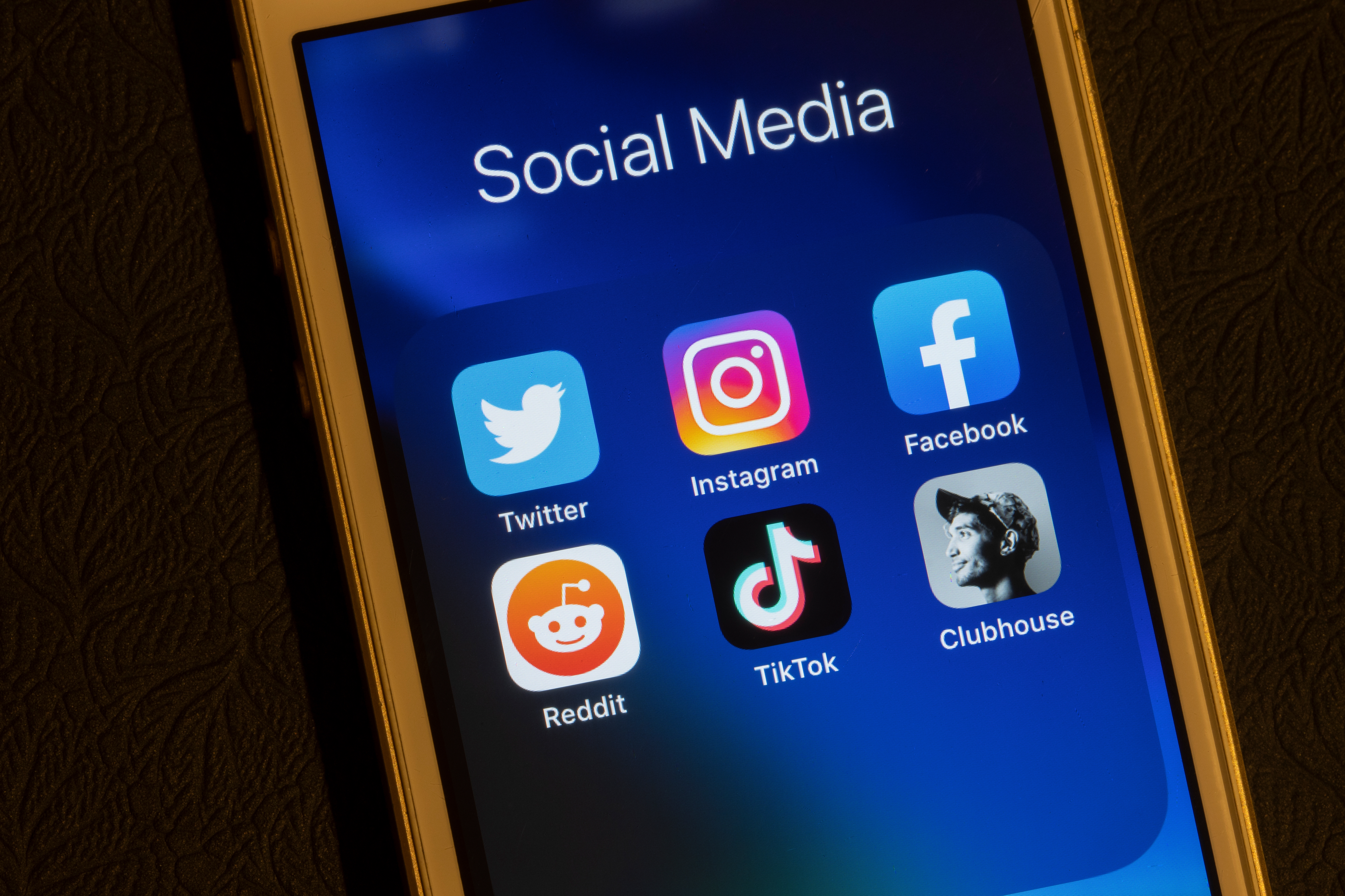 Smartphone screen showing social media apps: Twitter, Instagram, Facebook, Reddit, TikTok, and Clubhouse