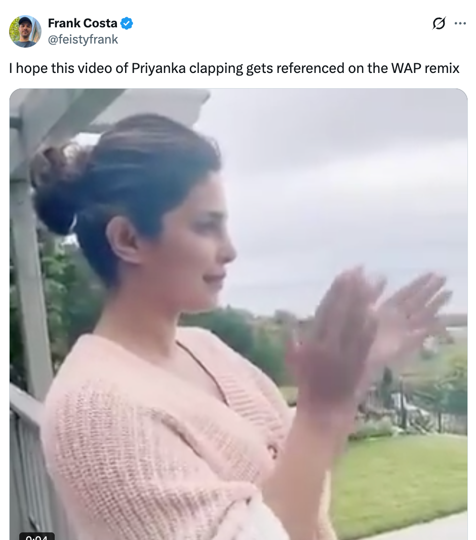 Person in a casual setting clapping hands outdoors, wearing a knit sweater, with a garden view in the background