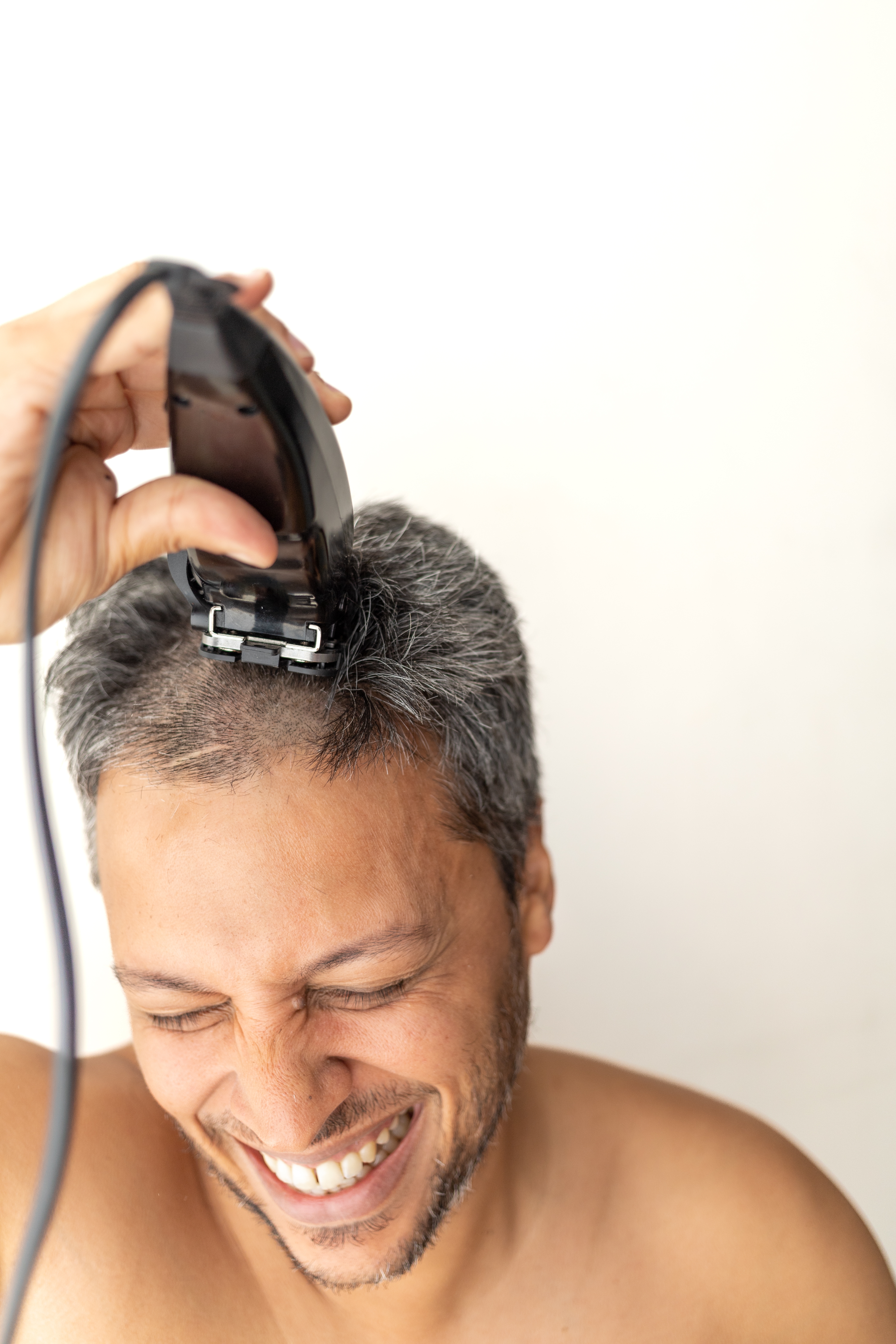 Person smiling while shaving their head with electric clippers, appearing happy and carefree