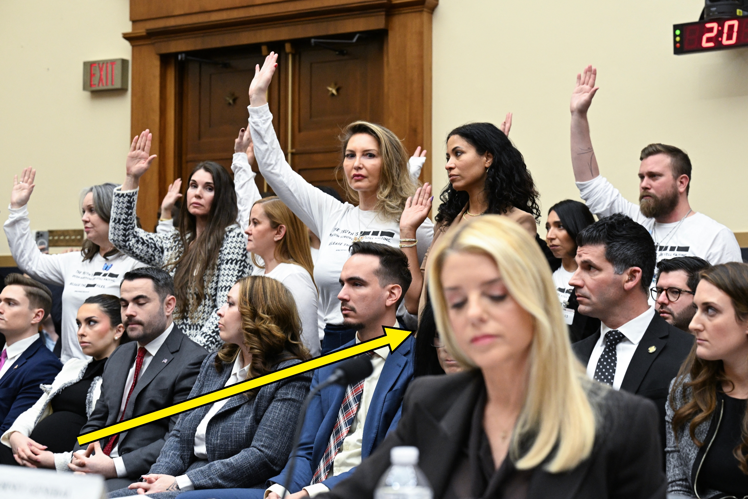 En gruppe individer, noen rekker opp hendene, i en formell høringssituasjon. Deltakere på første rad lytter oppmerksomt til saksgangen