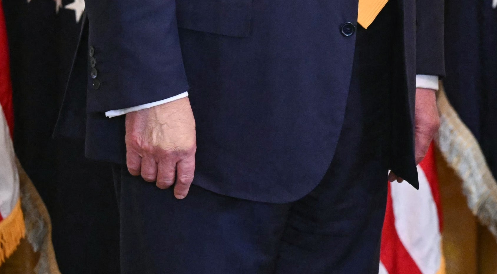 En person ved et podium snakker, med en passende mann som står i nærheten. De er i en formell setting med amerikanske flagg og presidentsegl