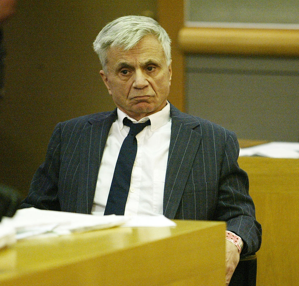 An older antheral successful a pinstripe suit sits successful a courtroom, looking pensive. Papers are connected the array earlier him