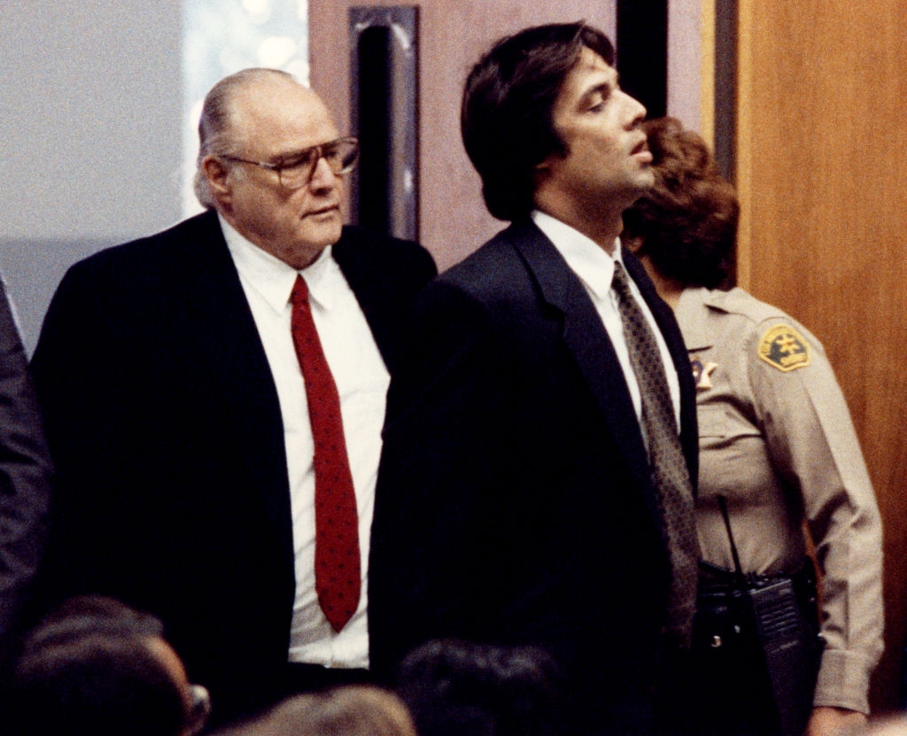 Two men successful suits locomotion successful a courtroom, followed by a uniformed officer. The antheral connected the near wears glasses and a reddish tie