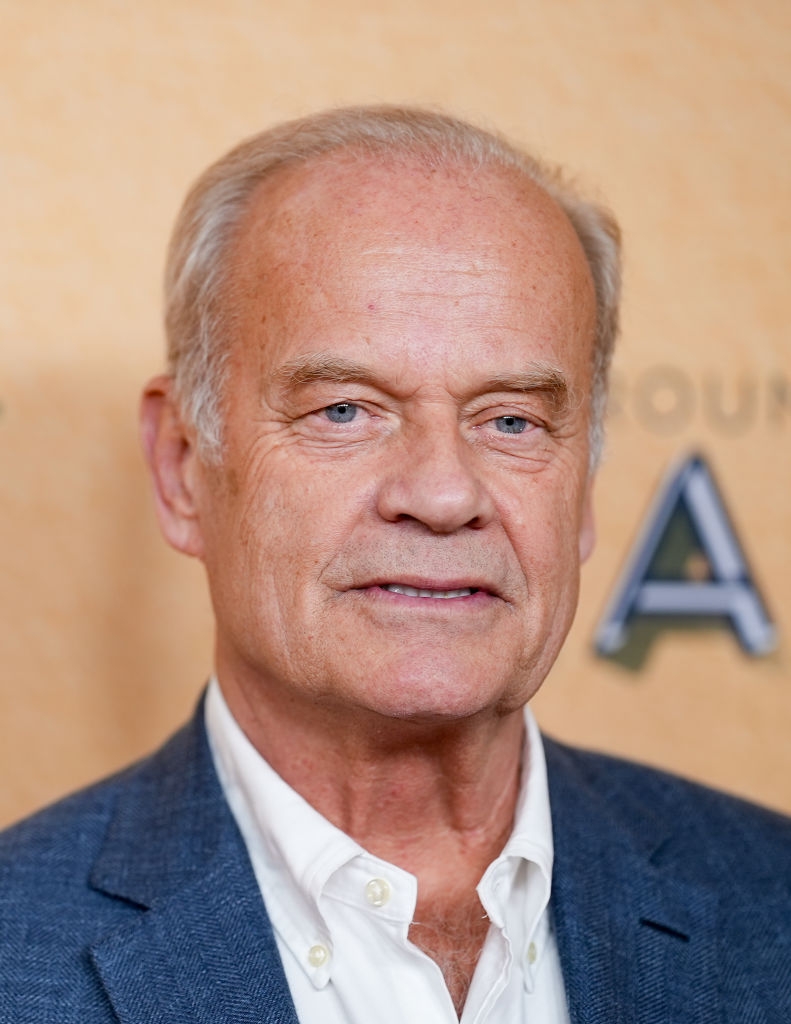 Person astatine an event, wearing a achromatic garment and bluish blazer, smiling somewhat successful beforehand of a inheritance with lawsuit text