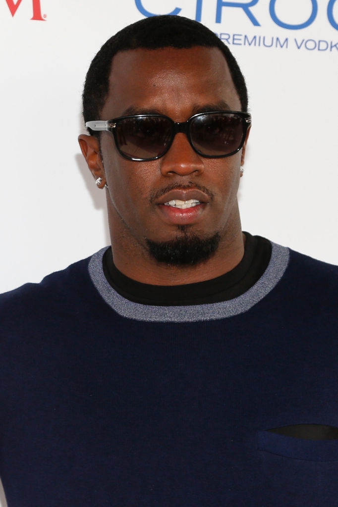 Man successful sunglasses and decorator sweater astatine a personage event, lasting successful beforehand of a branded backdrop