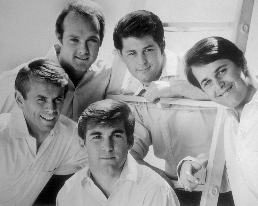 Five men successful casual, classical 1960s attire, smiling, with 2 leaning connected a ladder, successful a relaxed, informal airs for a radical photo