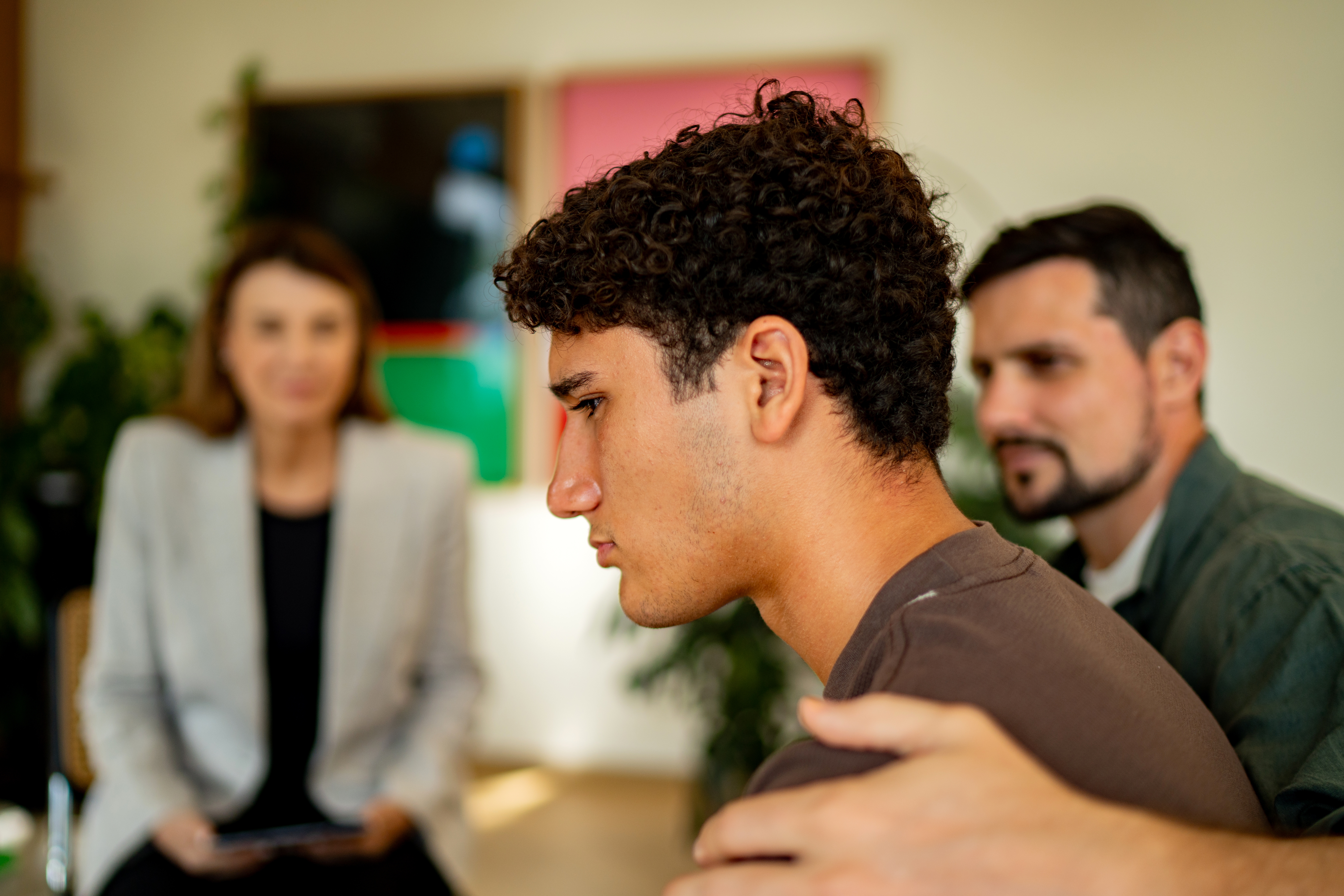 A young antheral   looks contemplative during a counseling league   with 2  adults, 1  offering enactment    with a manus  connected  his shoulder