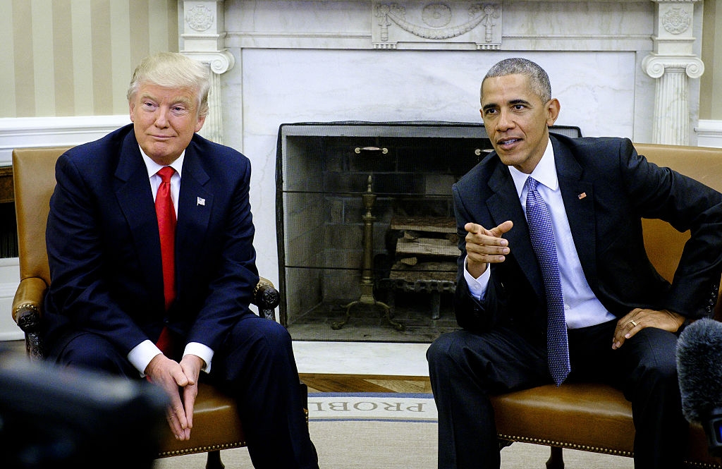 To menn i dress sitter på et kontor med en peis i bakgrunnen. Man snakker mens man gestikulerer; den andre lytter oppmerksomt