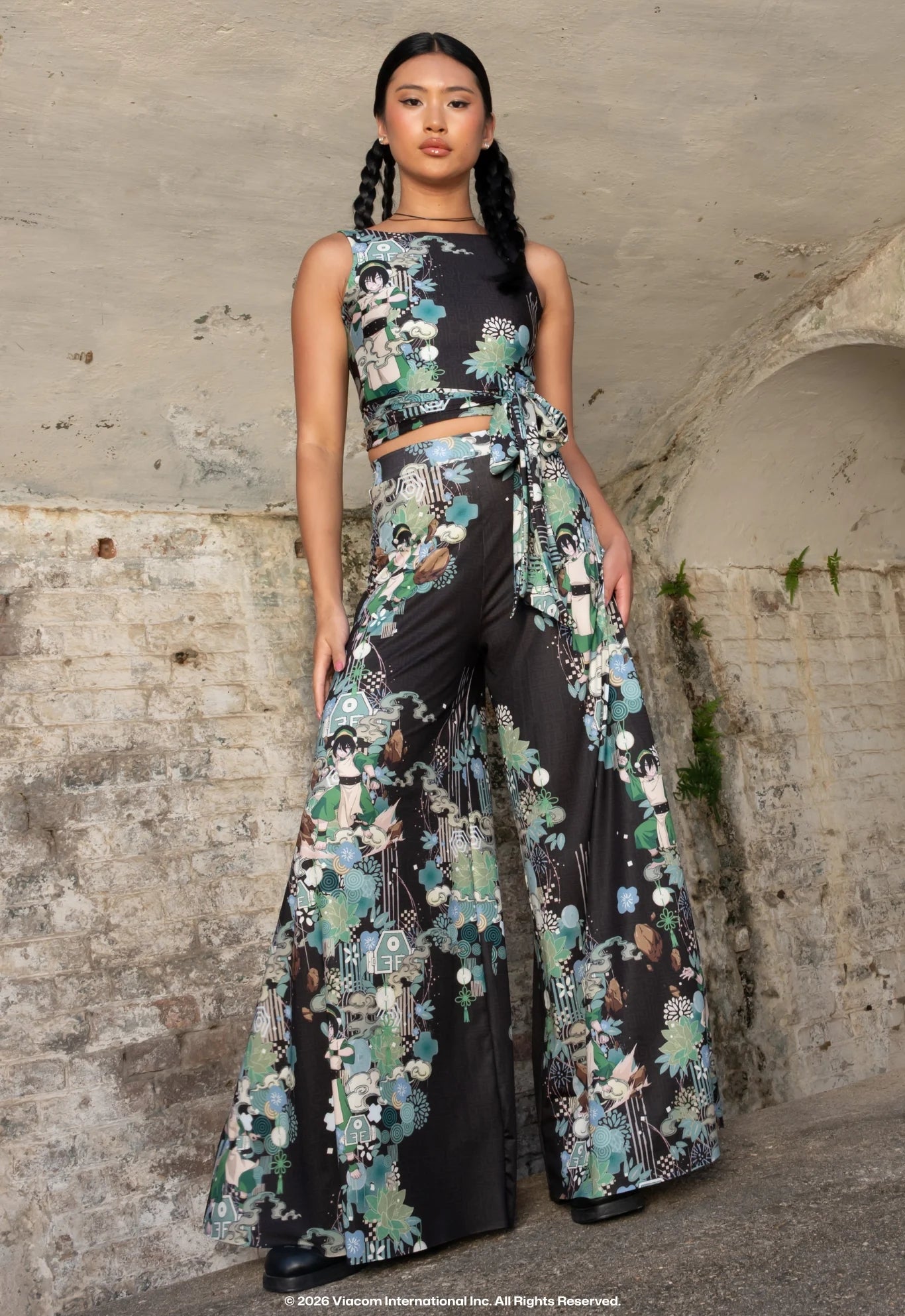 Person wearing a patterned sleeveless harvest  apical  and wide-leg pants lasting  confidently against a textured wall