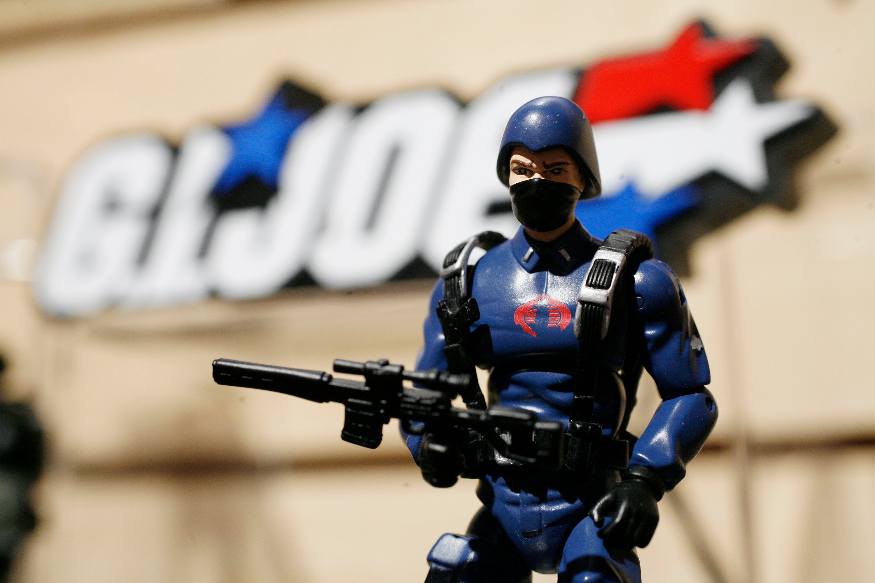 Action fig  holding a limb   stands successful  beforehand   of a blurred G.I. Joe logo, capturing a retro popular  civilization  theme