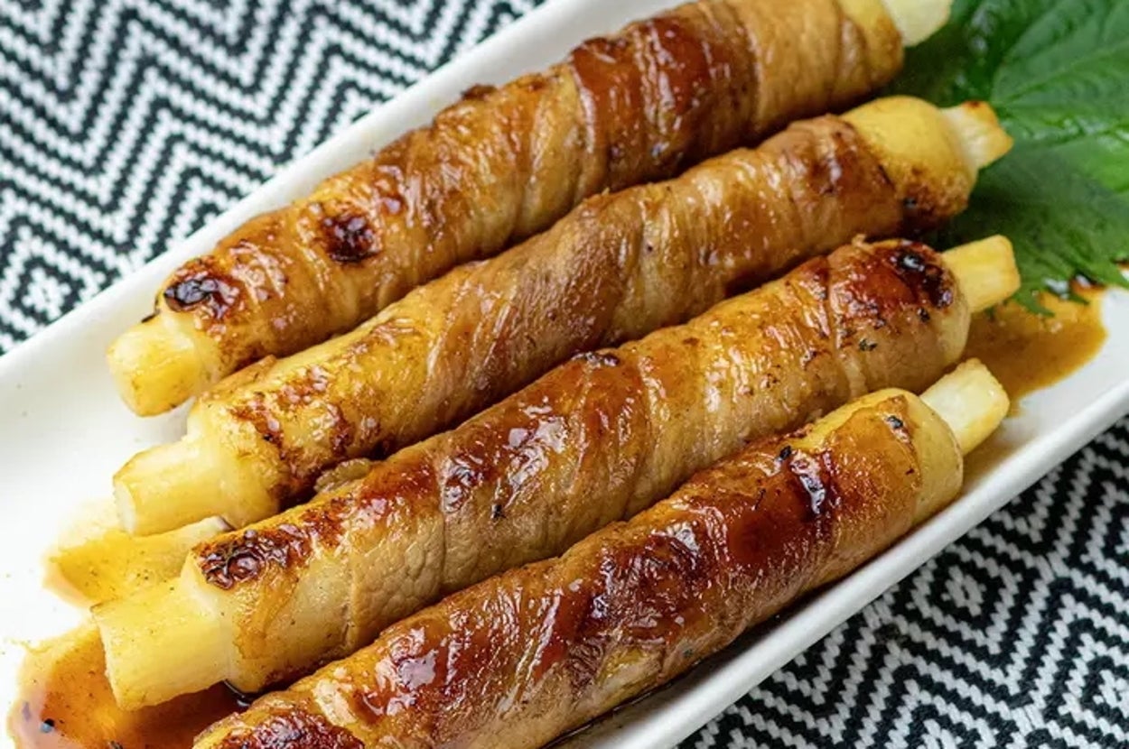 白いアスパラガスに肉が巻かれ、照り焼きソースがかかった料理。葉が添えられている。