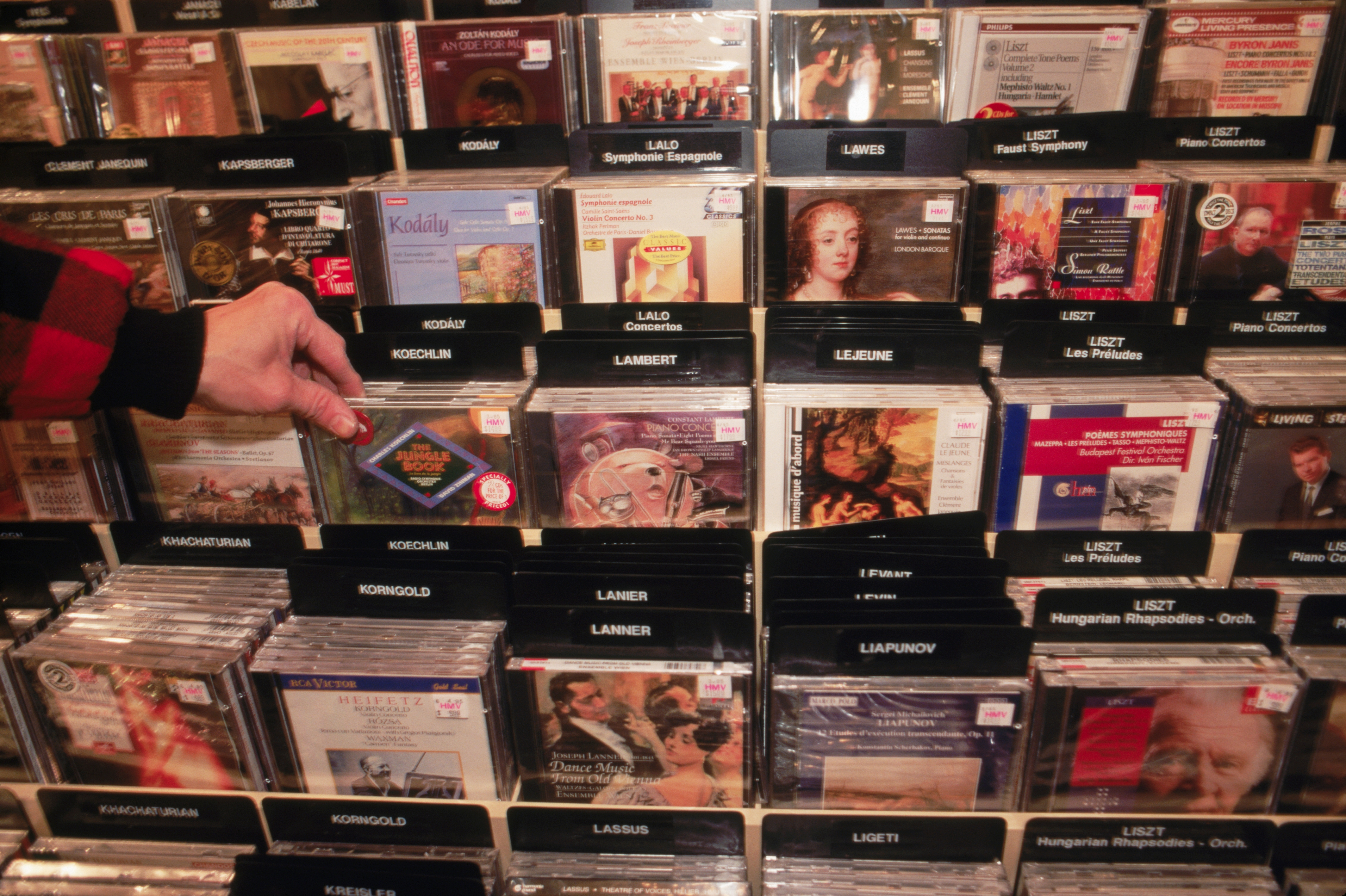 Hand selecting a classical euphony  CD from a store   show  filled with assorted  albums and composers similar  Liszt and Grieg
