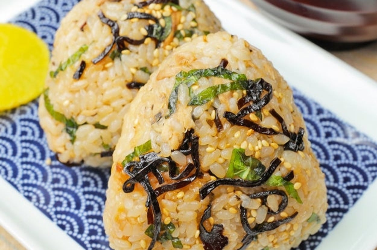 おにぎりが2個、白い皿の上に載っており、海苔とゴマがトッピングされています。横にはたくあんがあります。