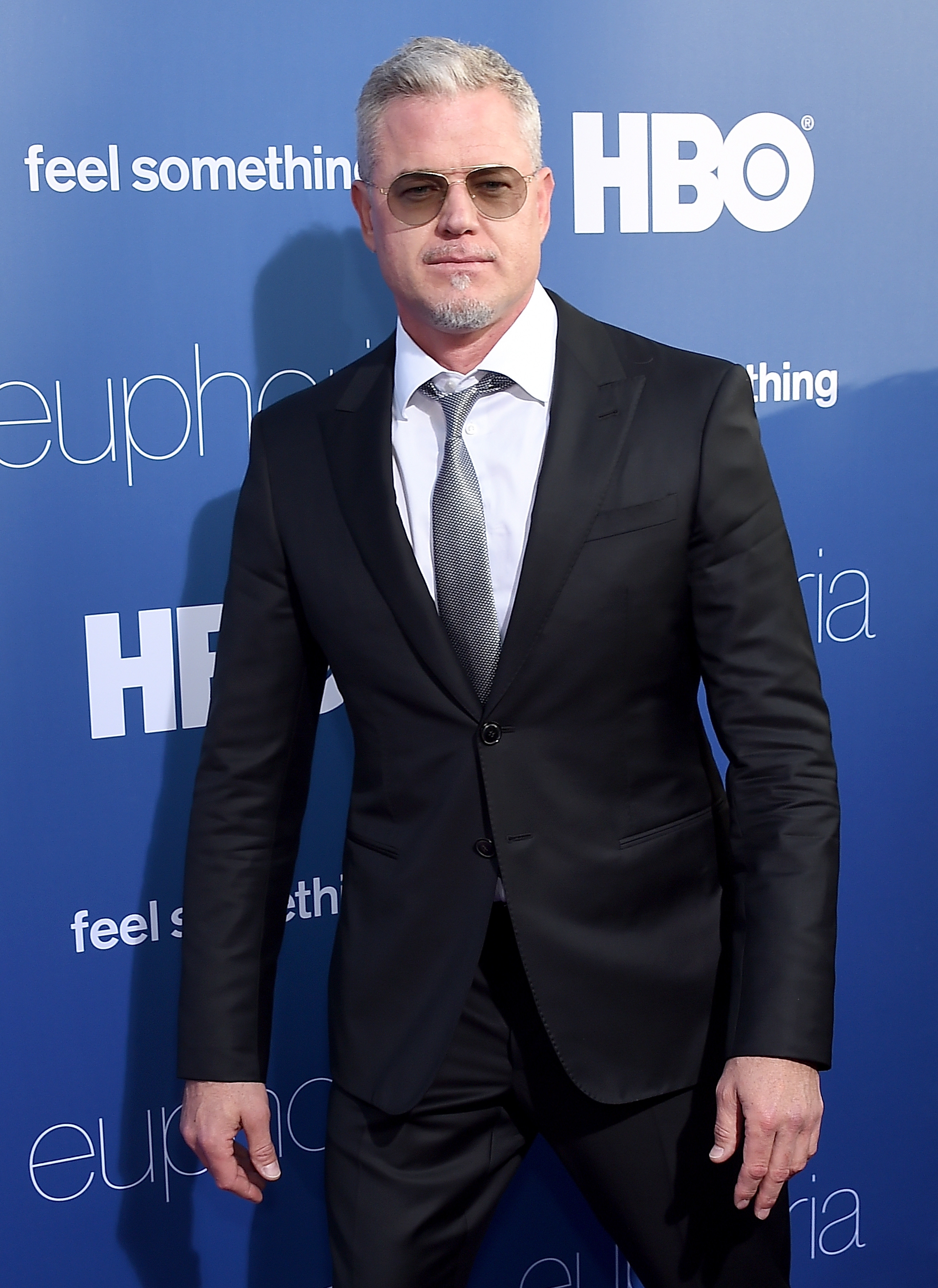 Person successful  a achromatic  suit   and necktie  stands connected  a reddish  carpet successful  beforehand   of a backdrop with "HBO" and "Euphoria" logos