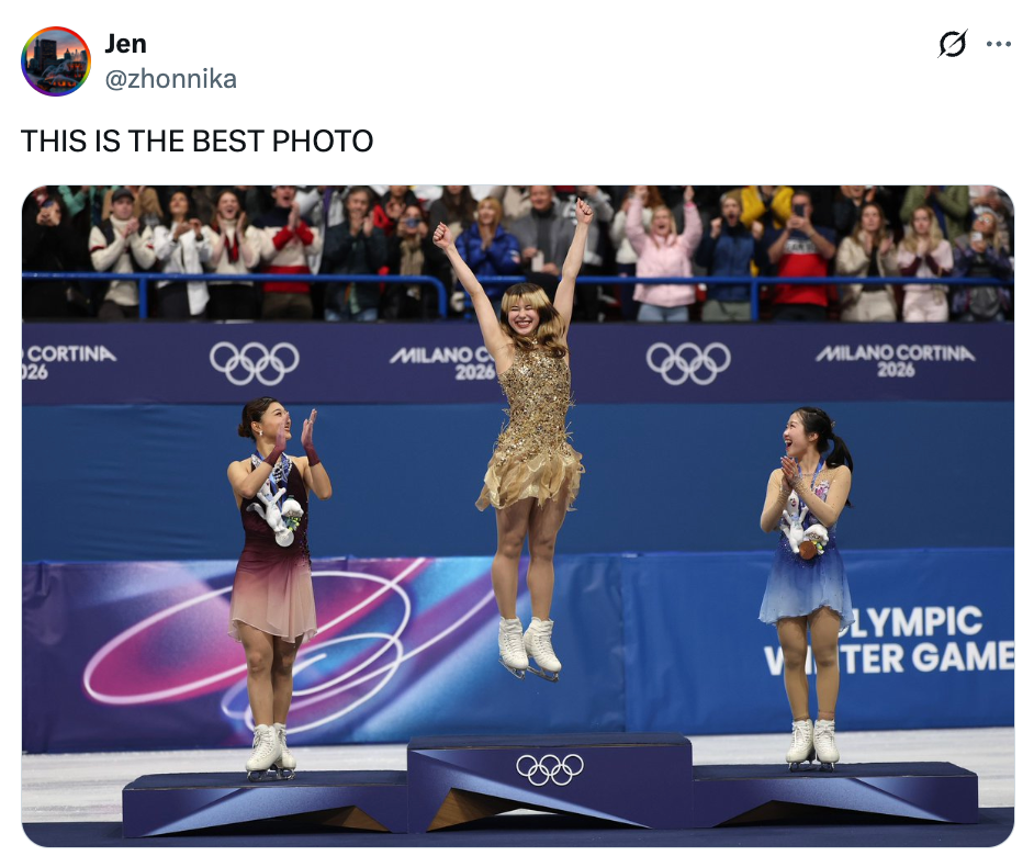Figure skater connected podium joyfully leaps successful solemnisation arsenic 2 skaters applauding, Olympic lawsuit backdrop, cheering crowd