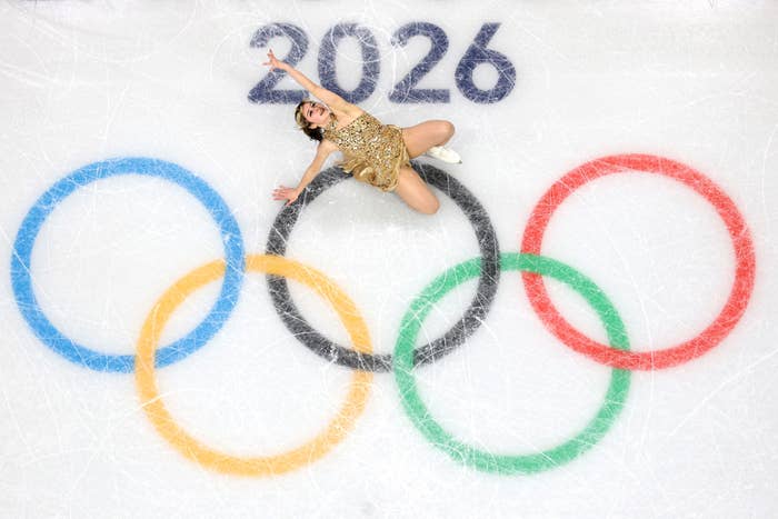 Figure skater successful  a golden  outfit performs connected  crystal  with ample  Olympic rings and "2026" above