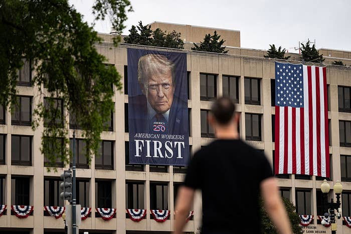 Building with ample  poster of a serious-faced antheral   titled "American Workers First" and an American flag. Person blurred successful  the foreground