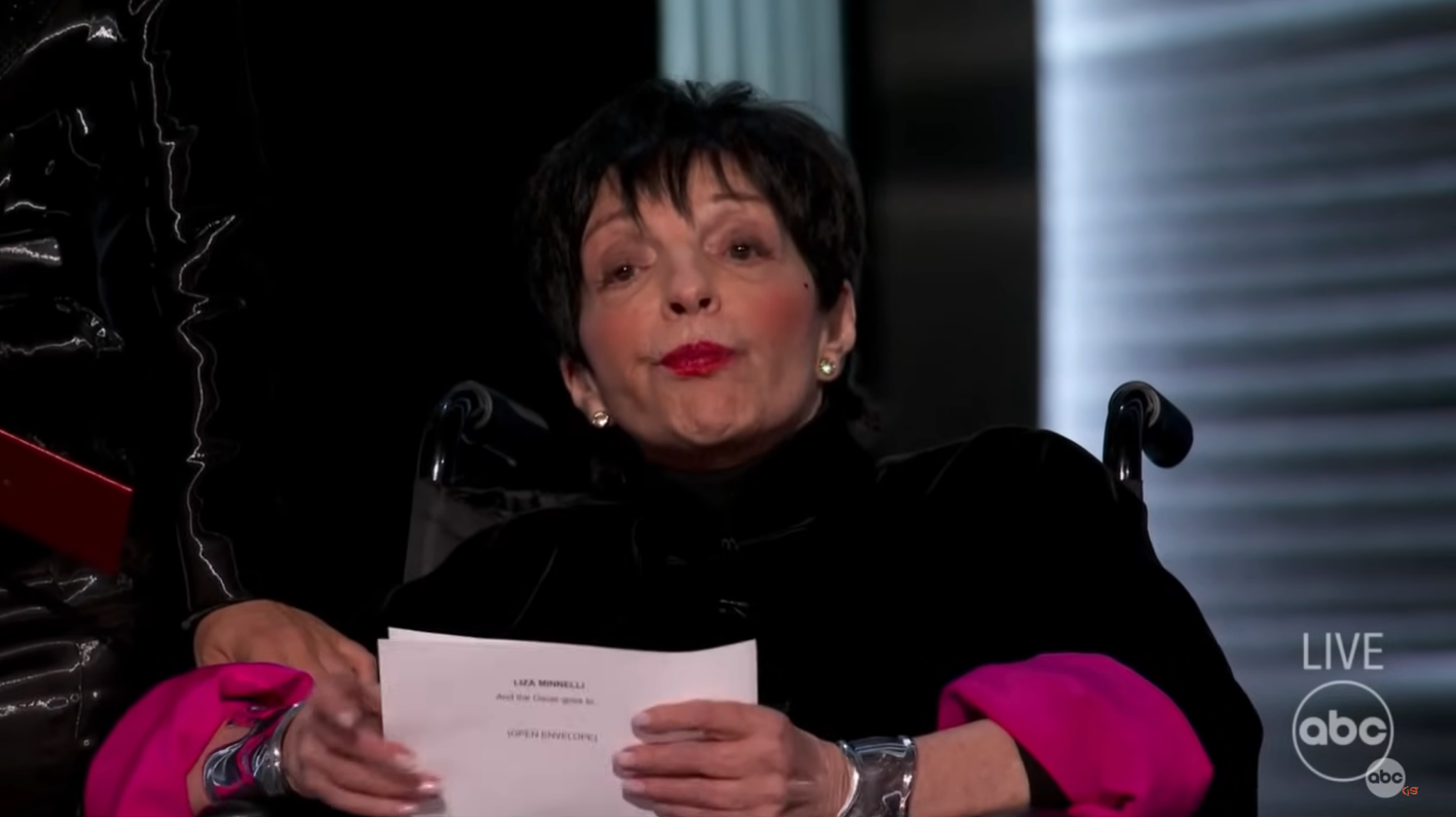 Liza Minnelli successful  a wheelchair holding a document, wearing a stylish outfit with bold sleeves