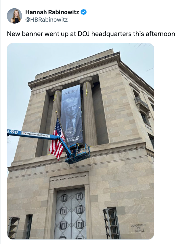 A banner show  is being installed astatine  the U.S. Department of Justice office  by workers connected  a assistance   adjacent  to the American flag