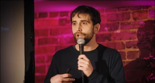Person holding a microphone, mid-speech, successful  beforehand   of a ceramic  partition  with purple lighting. Casual attire
