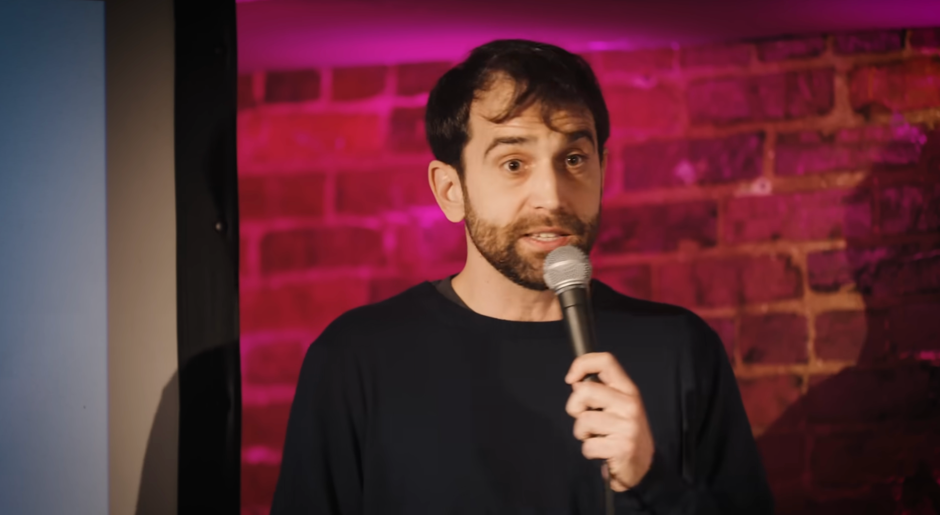 A idiosyncratic   is performing stand-up drama  connected  stage, holding a microphone with a ceramic  partition  backdrop