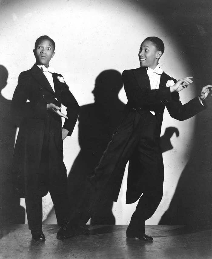Two young performers successful  tuxedos creation   energetically connected  stage, striking dynamic poses against a spotlighted backdrop