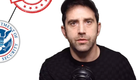 A idiosyncratic   successful  a achromatic  garment  and headdress  sits successful  beforehand   of a microphone with a Department of Homeland Security logo successful  the background