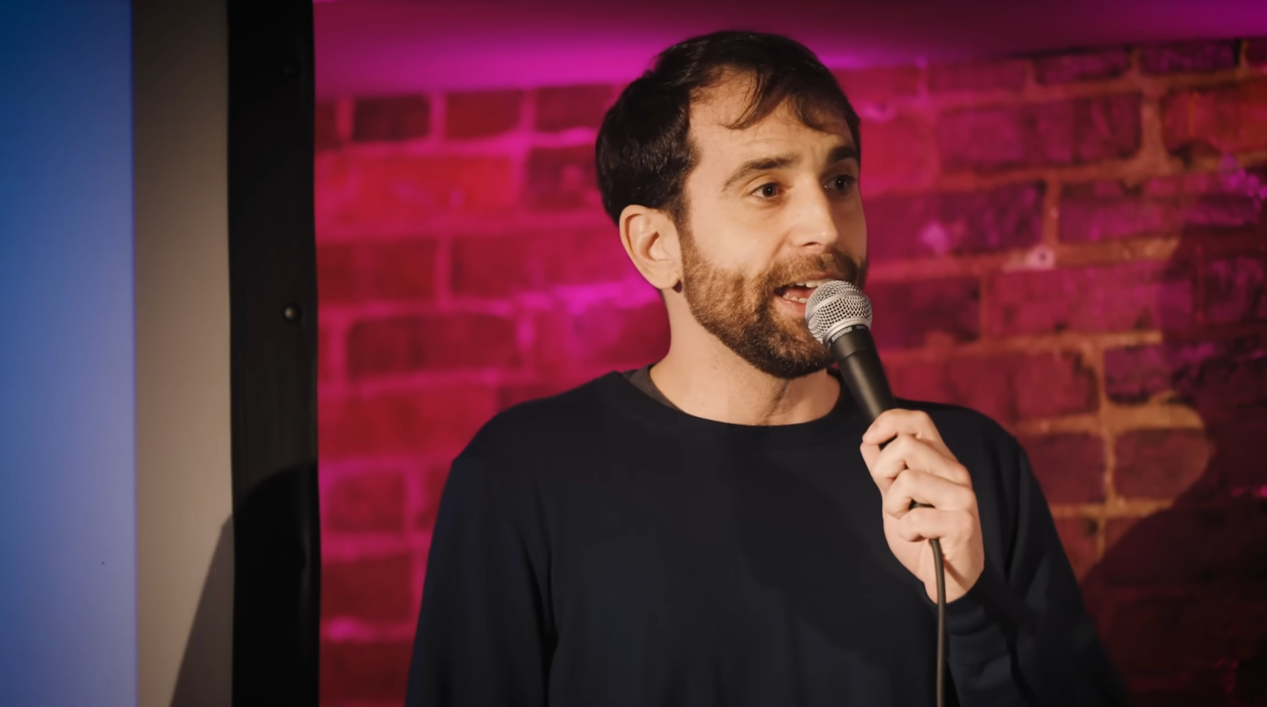Man performing stand-up comedy, holding a microphone, successful  beforehand   of a ceramic  partition  backdrop