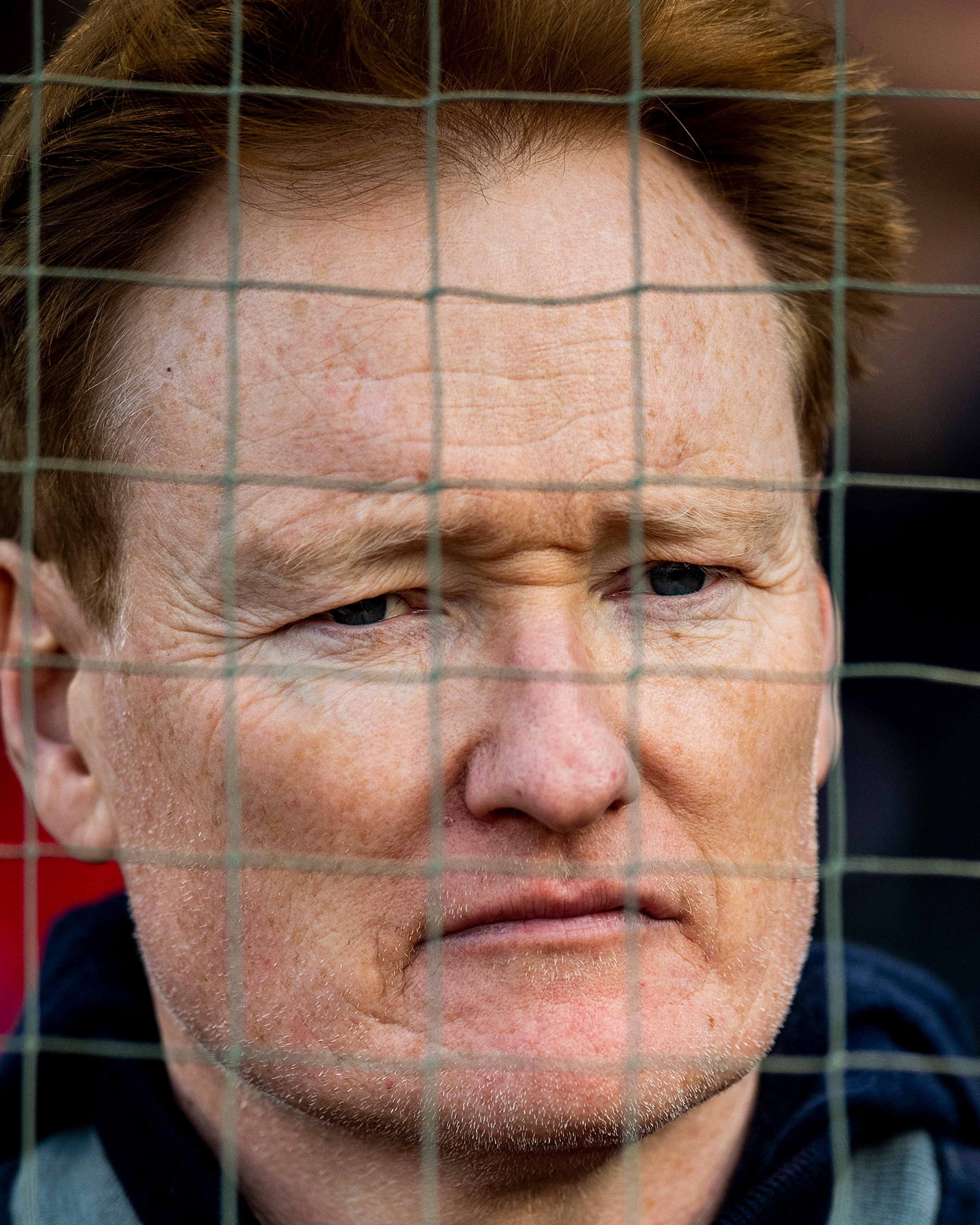 Conan O'Brien bak et trådgjerde, ser ettertenksomt over barrieren