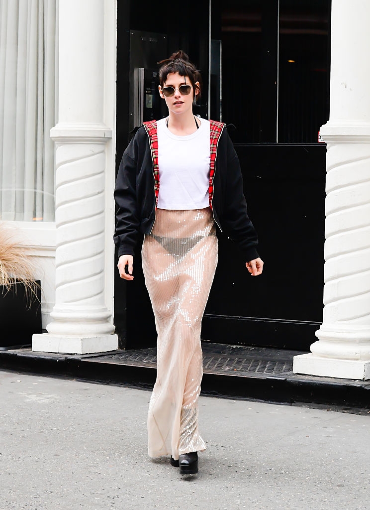 Person walking connected the thoroughfare wearing a sequined maxi skirt, achromatic t-shirt, and achromatic overgarment with a reddish plaid lining