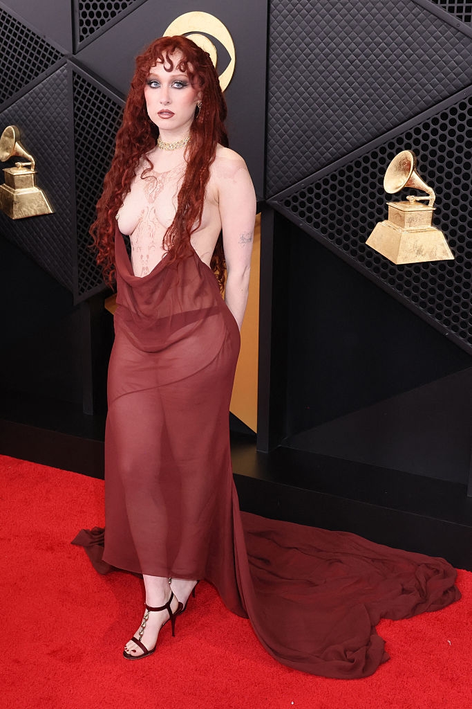 Person connected reddish carpet successful a flowing, semi-transparent gown with a long, unfastened front. They person long, wavy hairsbreadth and are posing adjacent grant statues
