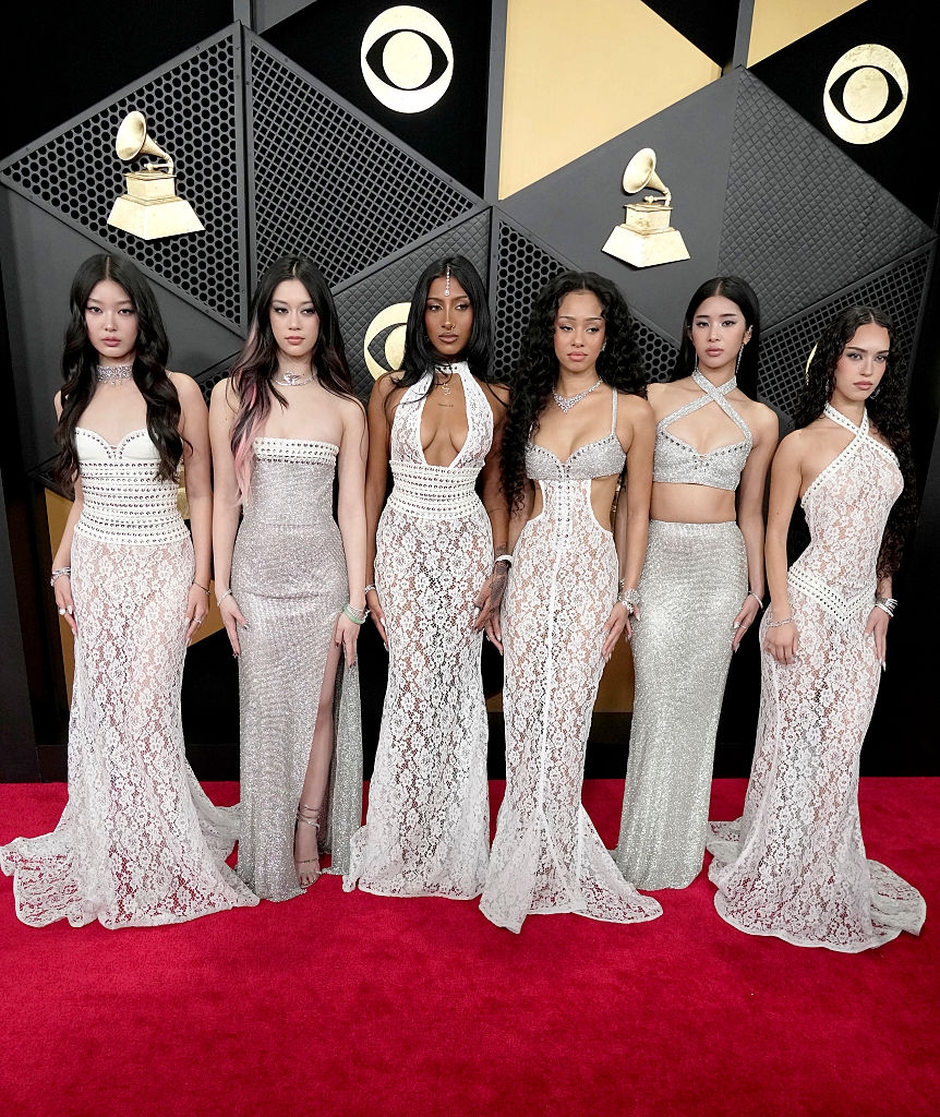 Six women basal connected a reddish carpet successful matching floor-length gowns with intricate lace designs, posing for photos astatine an event