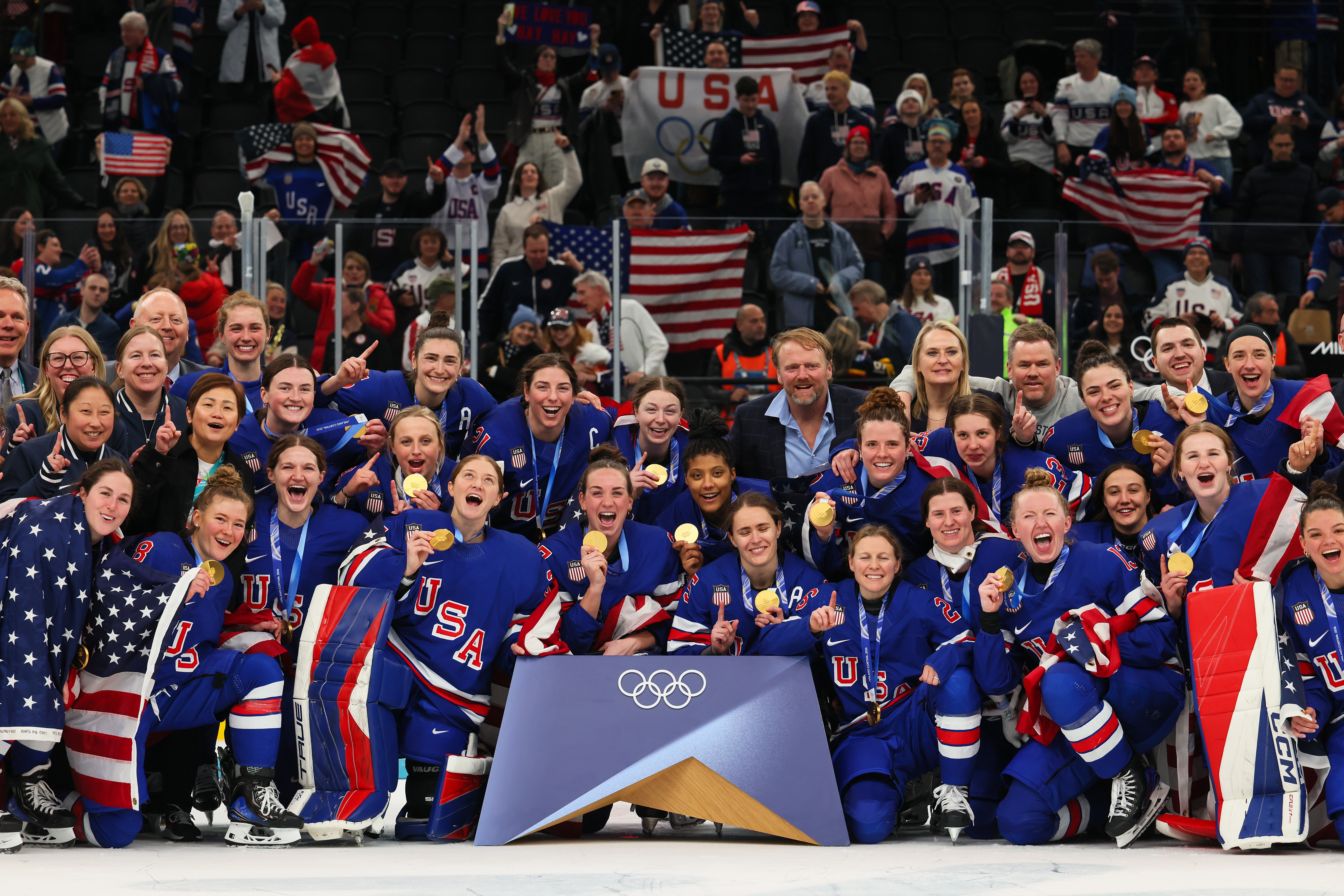 USA women's crystal hockey squad celebrates winning with medals; fans cheer successful the background, holding flags and banners