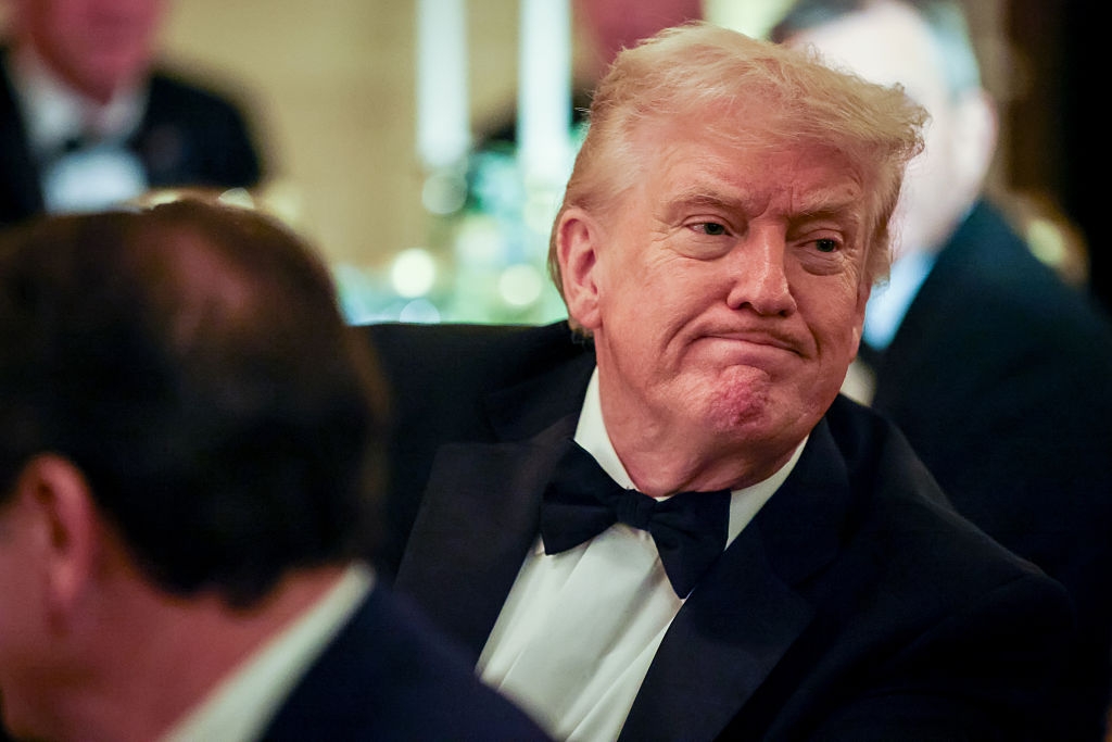 Person successful a ceremonial suit with a bow tie, sitting astatine a eating event, looking to the broadside with a neutral expression