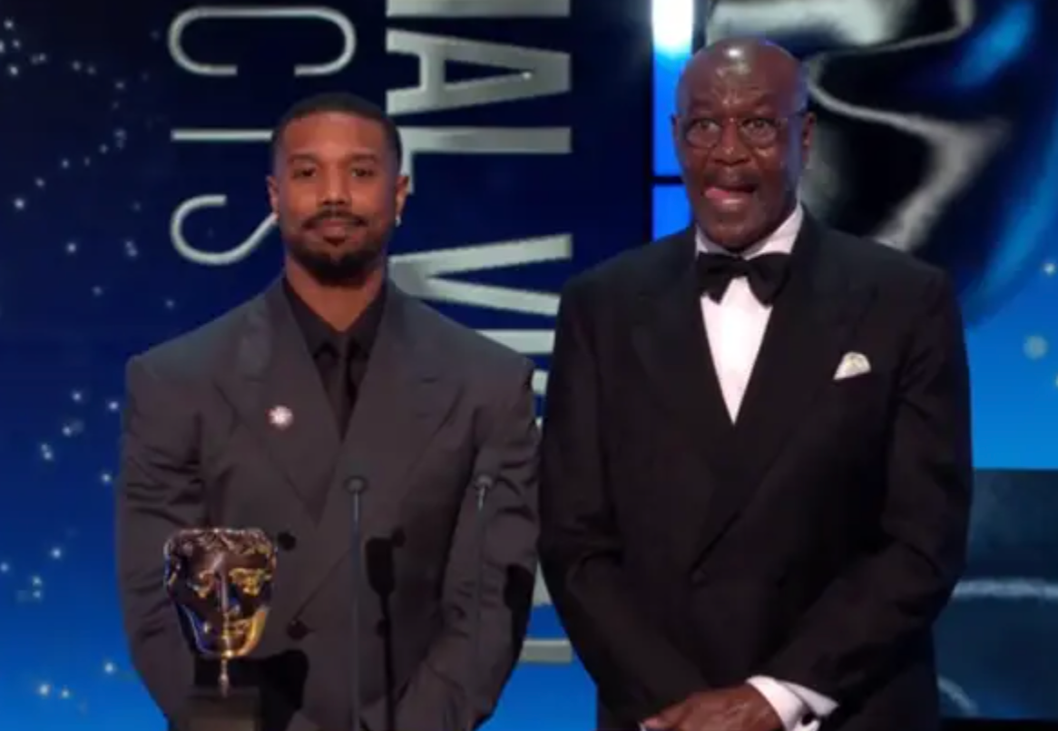 Two men connected  signifier    successful  ceremonial  suits astatine  an grant  ceremony, lasting  successful  beforehand   of a microphone with a bluish  backdrop