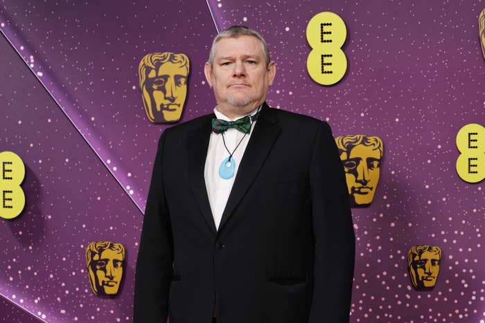 Person wearing a achromatic  suit   and bow tie, lasting  successful  beforehand   of a backdrop with BAFTA logos
