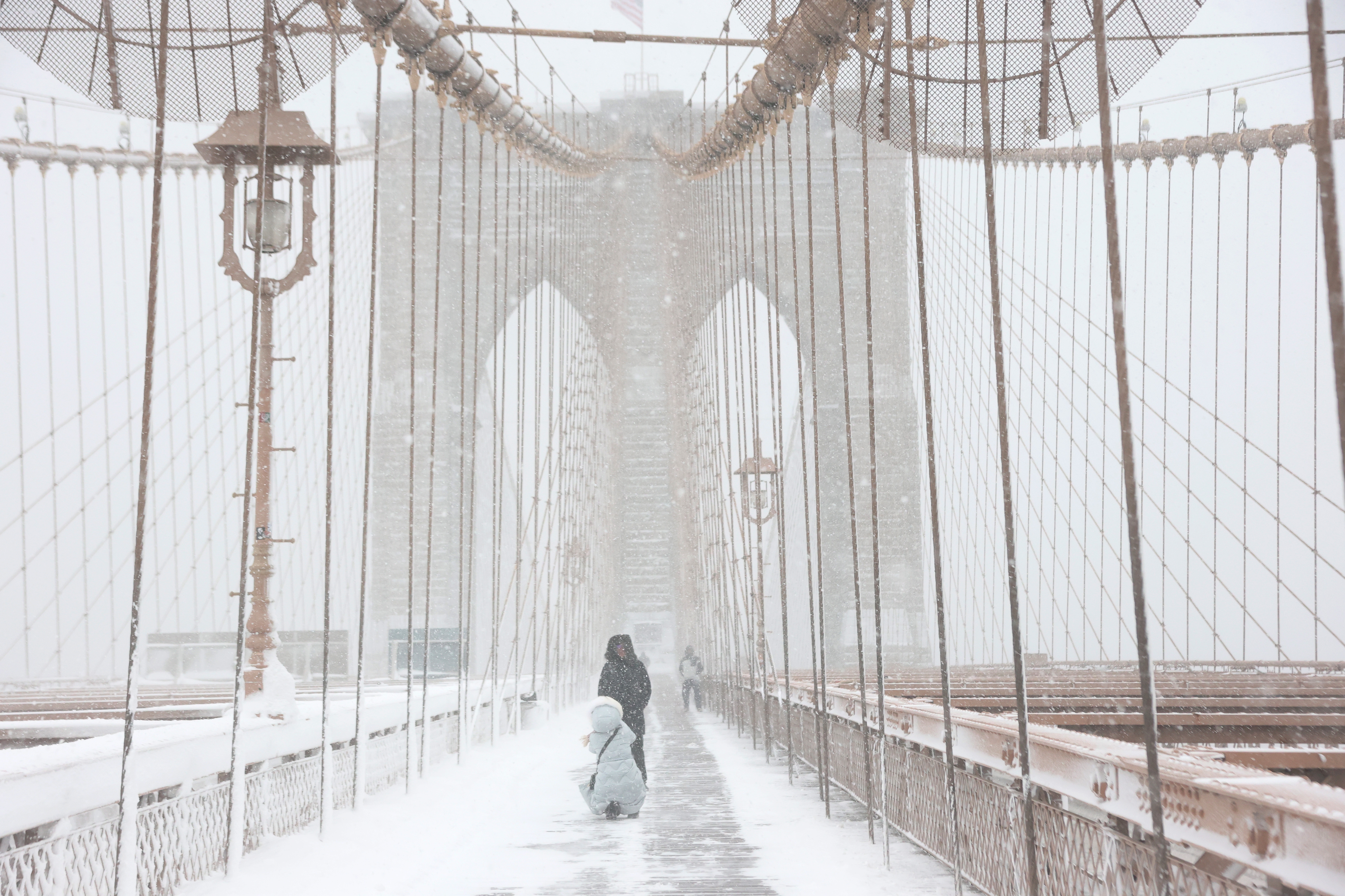 Folk som går på en snødekt bro under kraftig snøfall, med begrenset sikt på grunn av værforholdene