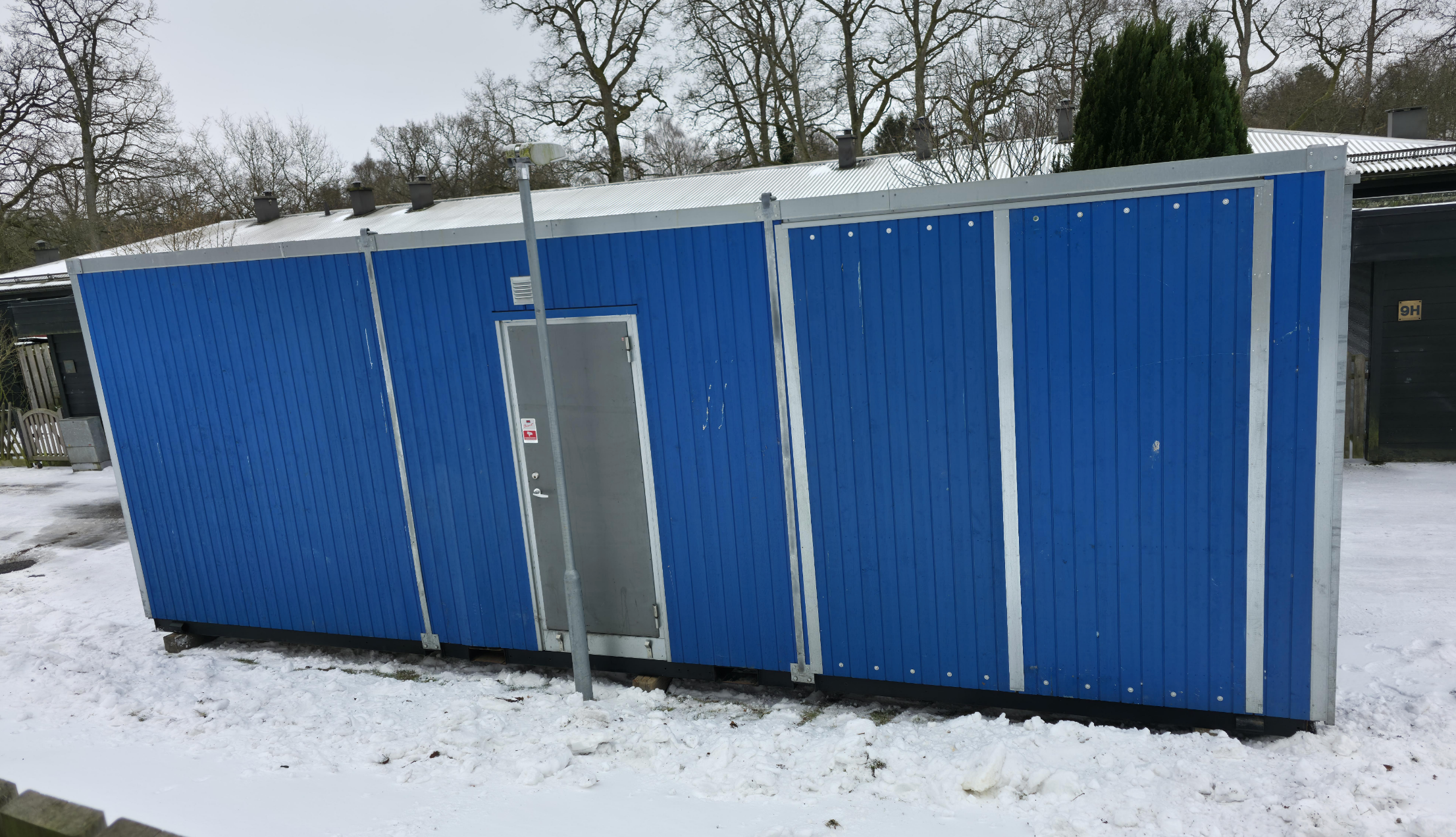 A blue portable building with a closed metal door blocked by a pole