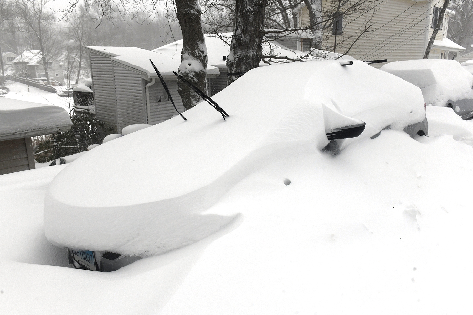 Bil begravd under snø med vindusviskere hevet i et snødekt boligområde