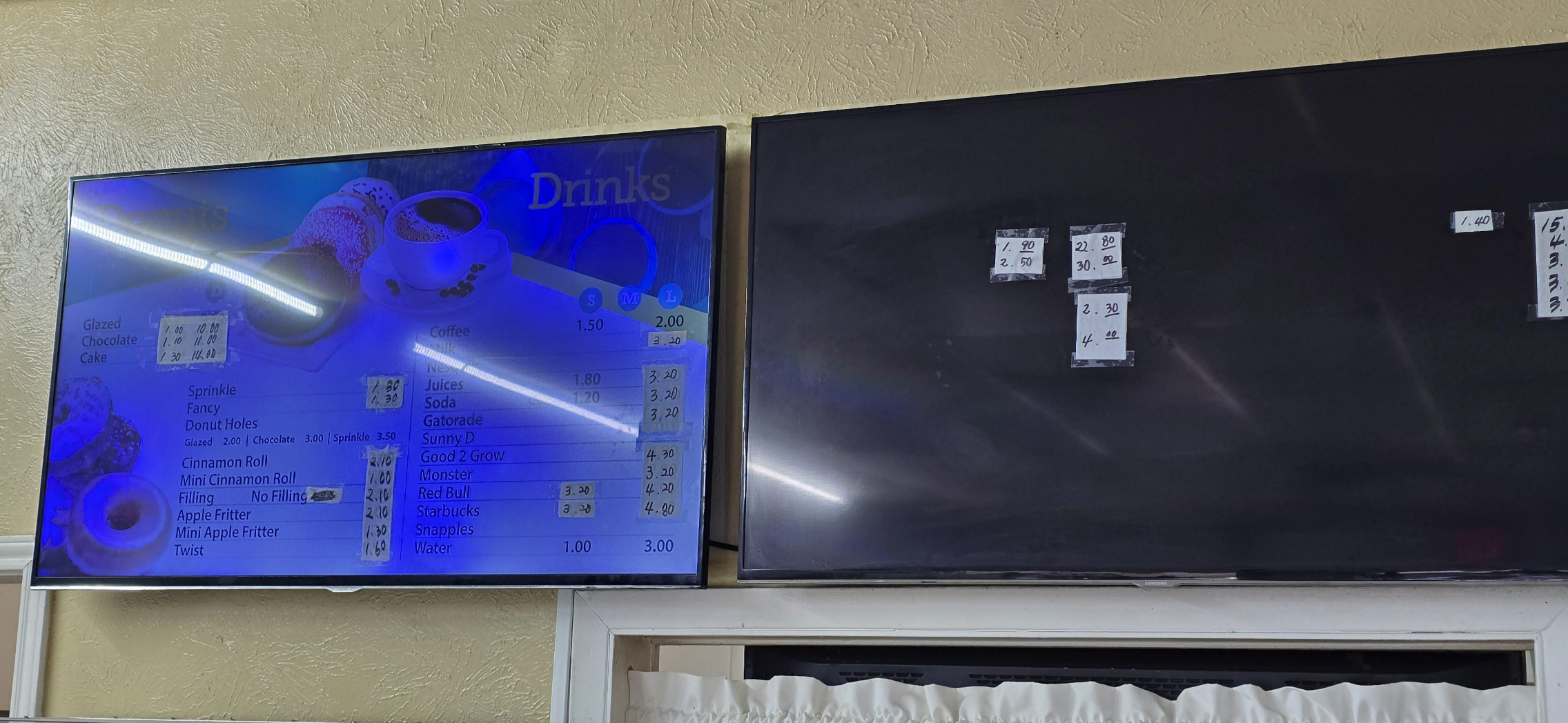 Two digital menu screens, one partially visible with drinks listed and the other off or blank with prices taped on