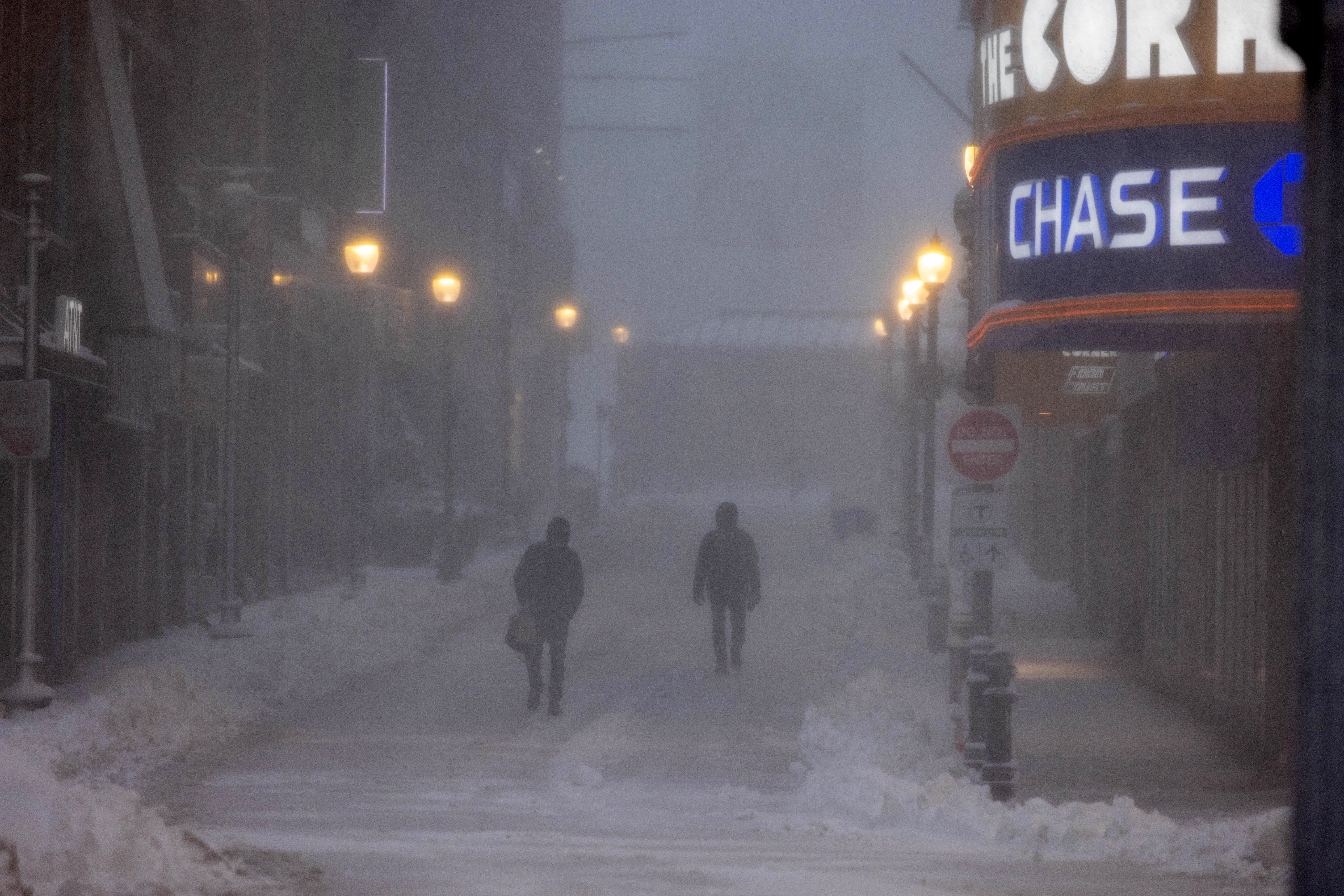 To personer går ned en snødekt, svakt opplyst bygate, og kjemper mot sterk vind og dårlig sikt