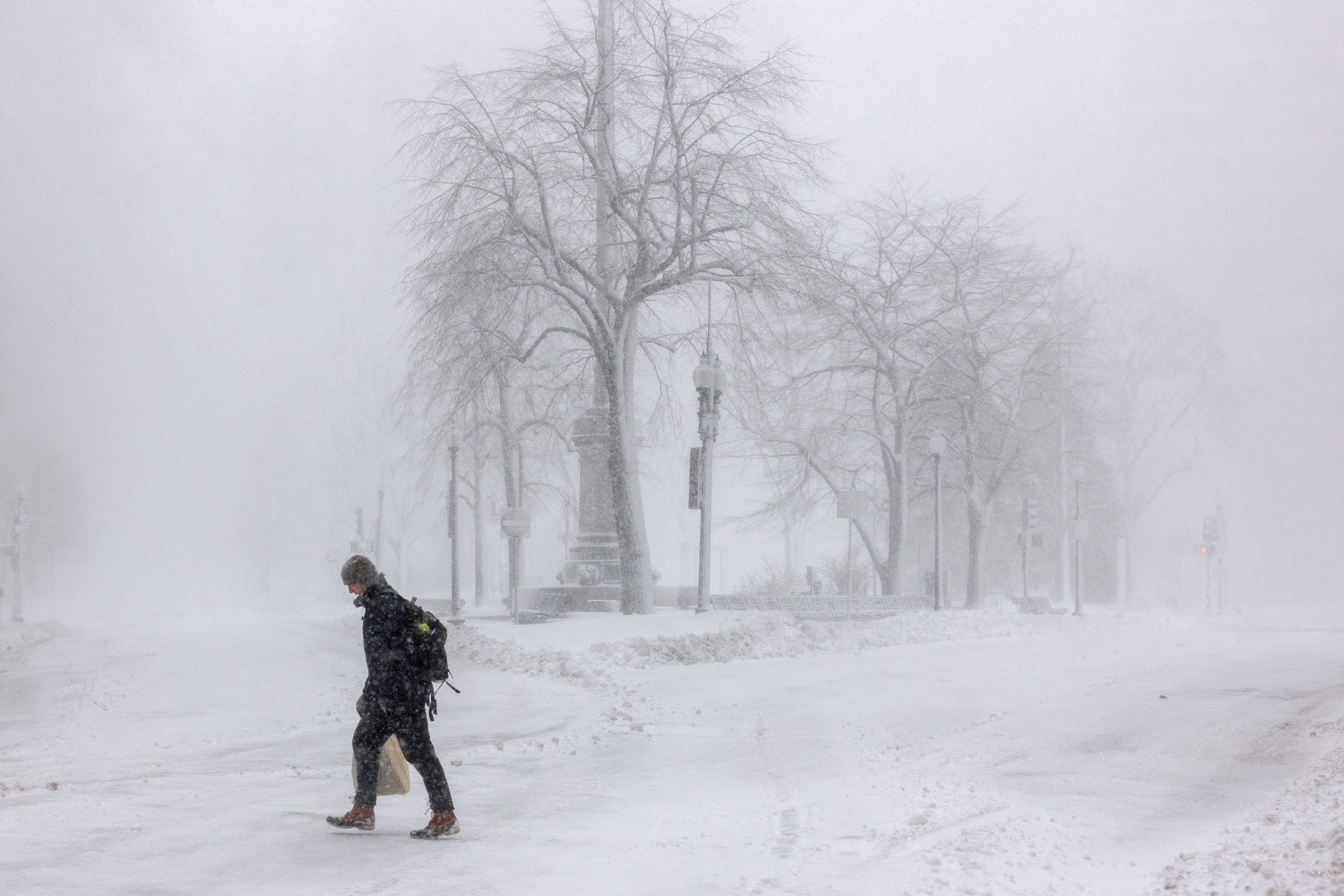 Person går gjennom tung snø i en vinterpark. Trær og benker er knapt synlige i den snødekte disen