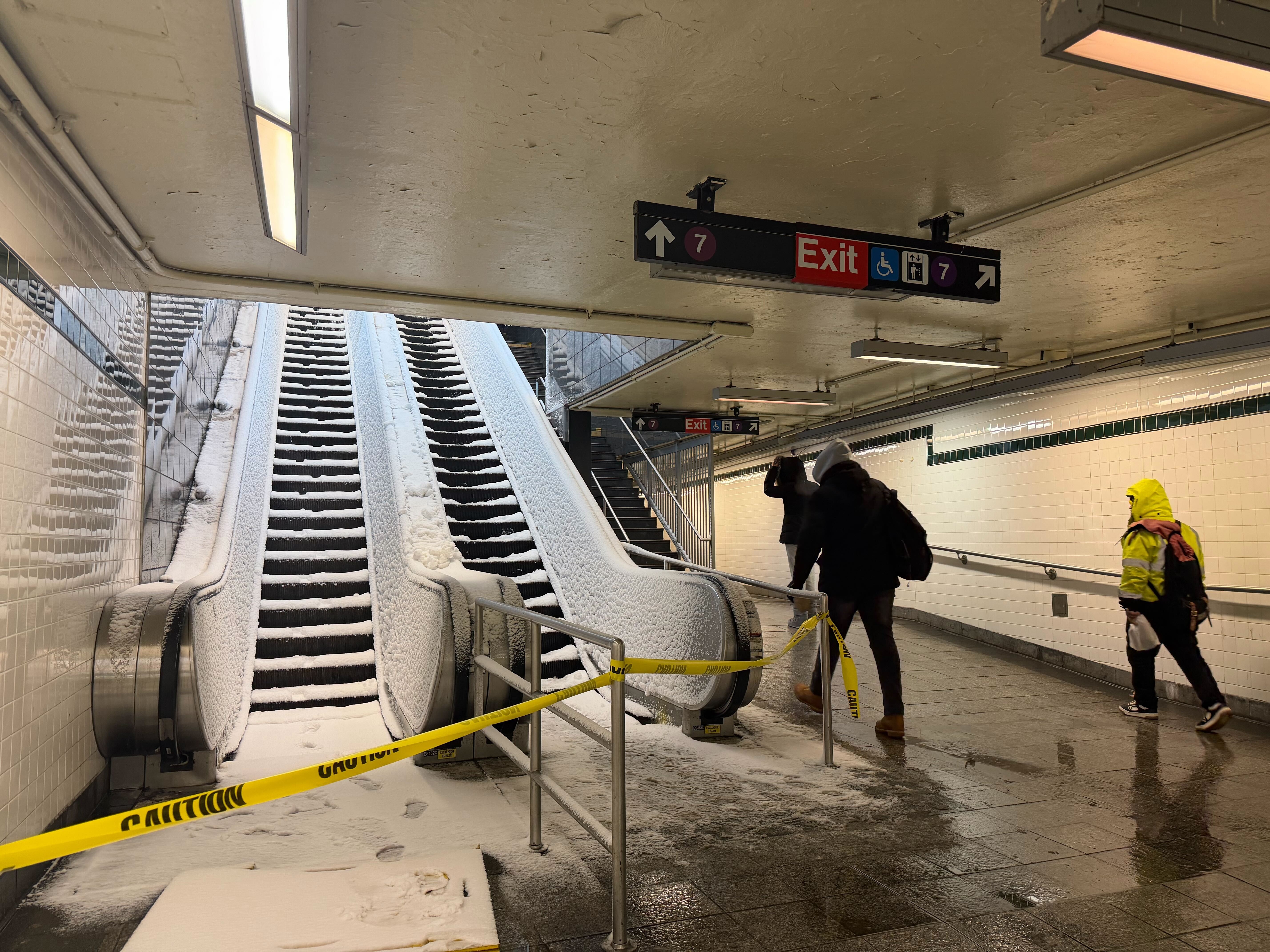 T-bane rulletrapp dekket av snø med forsiktig tape som blokkerer inngang; folk navigerer rundt det
