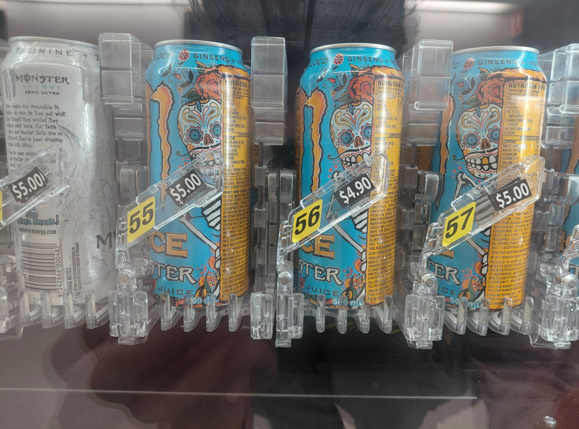 Energy drink cans with vibrant designs are displayed in a vending machine. Prices are $5.00 except for one that is $4.90 even though it's the same one