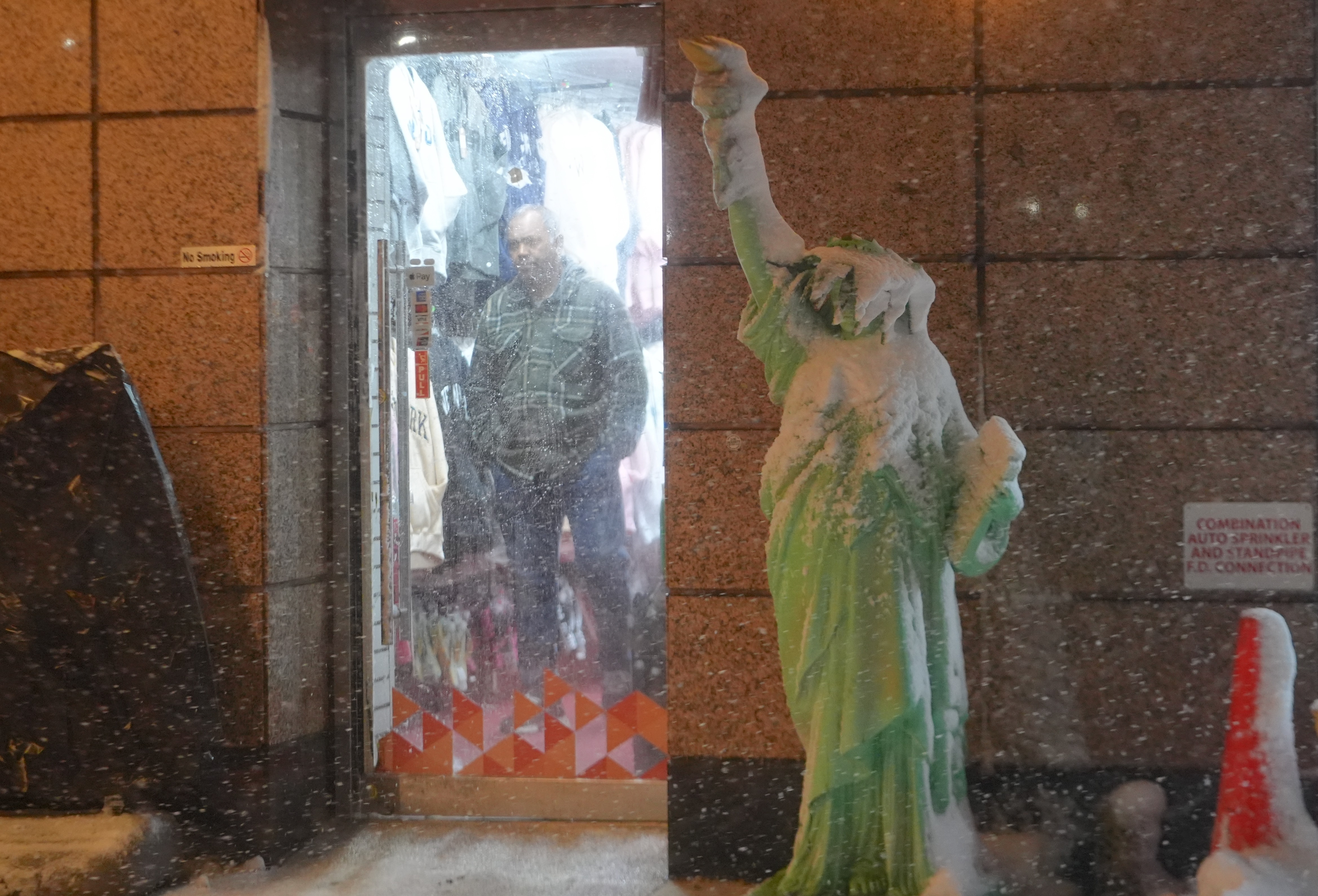 Mann som ser ut av døren mens snøen faller på en kopi av en hodeløs Frihetsgudinnen