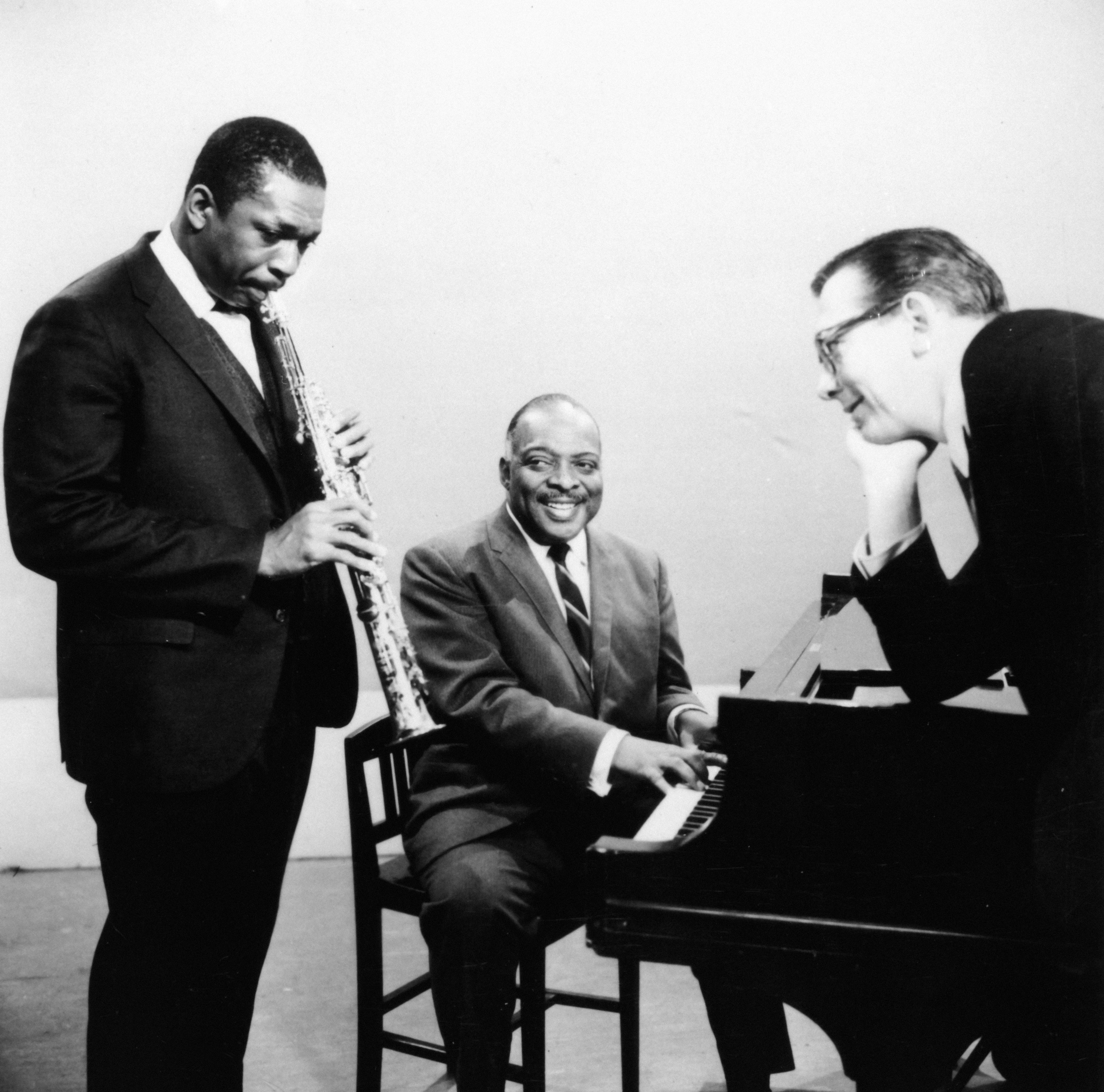  1  plays the saxophone, 1  plays the piano, and 1  leans connected  the piano, smiling and engaged