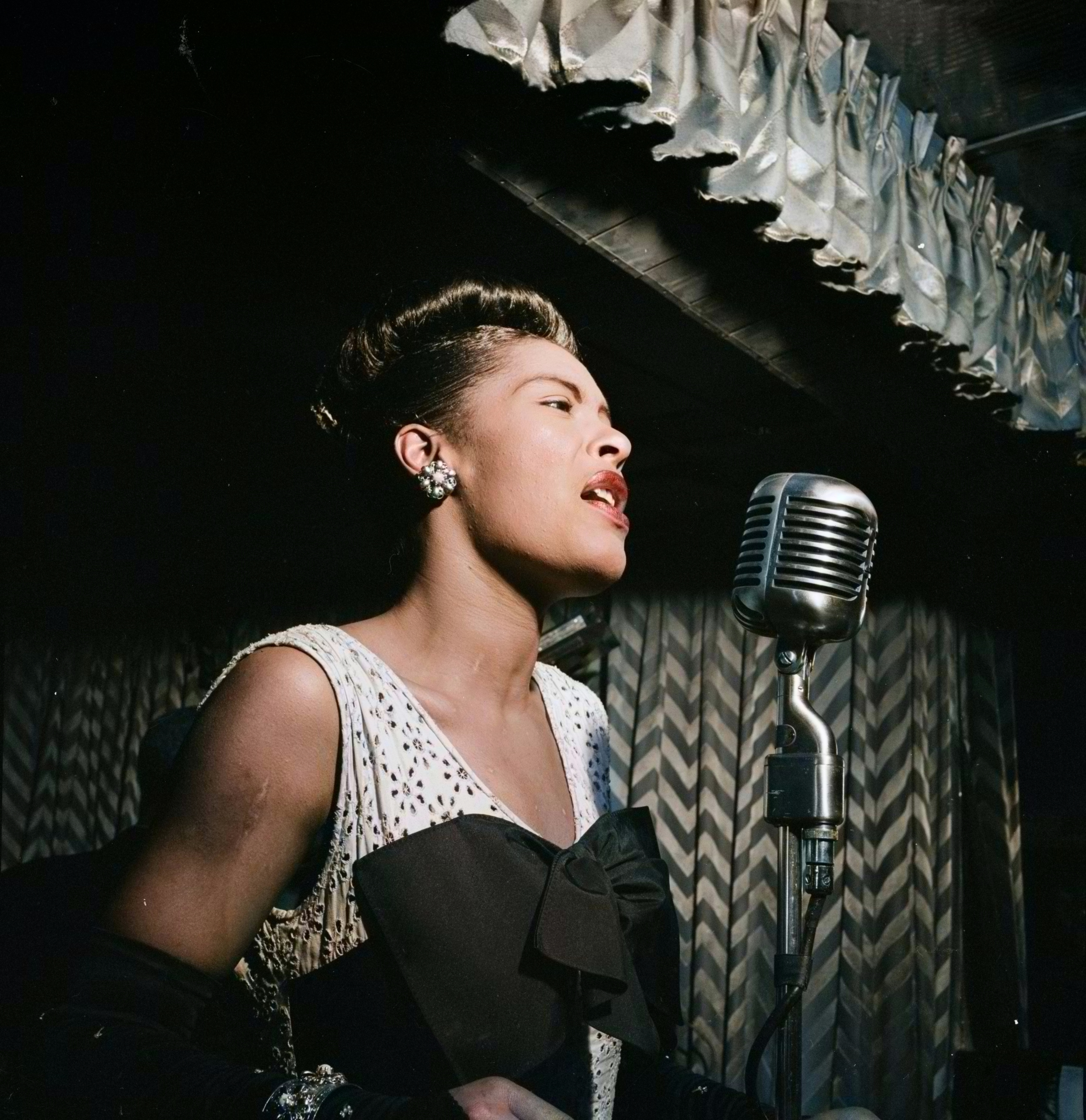 Woman successful  elegant formal  sings into vintage microphone connected  stage, with chevron patterned curtain successful  the background