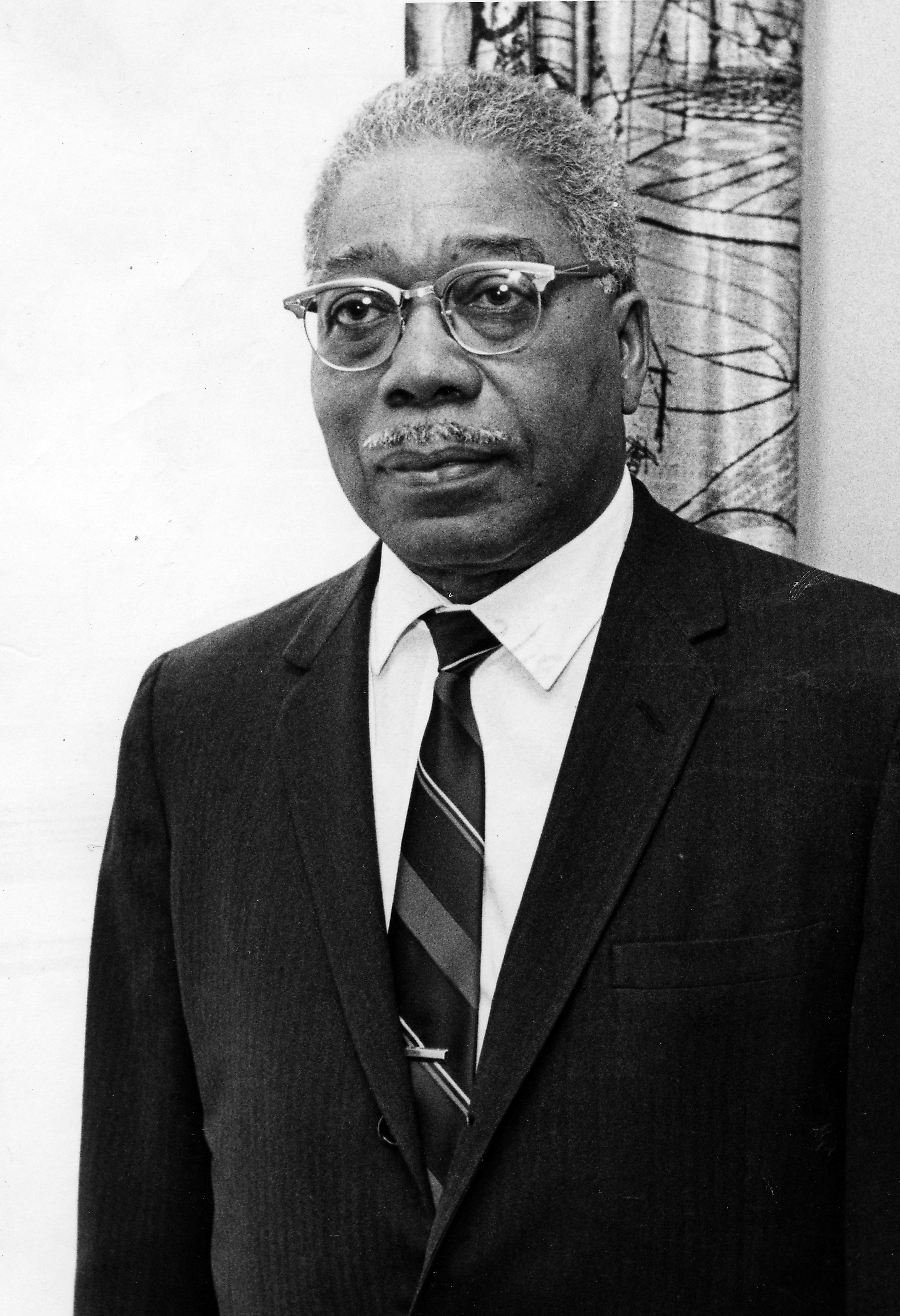 An older antheral   with glasses, a mustache, and a superior   look  wears a suit   and striped tie, lasting  indoors