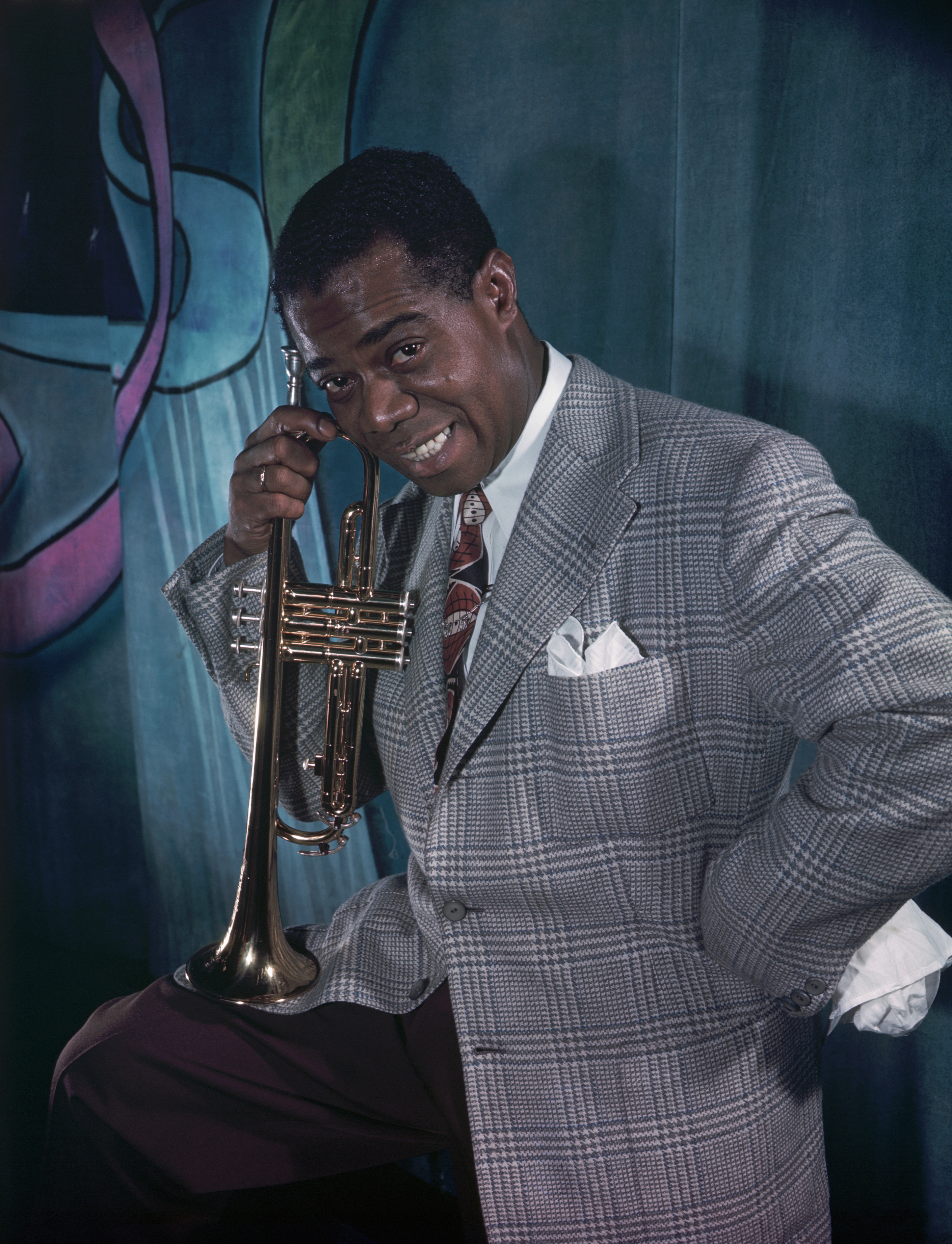 A instrumentalist  successful  a checkered suit   poses with a trumpet, smiling, successful  beforehand   of an abstract backdrop